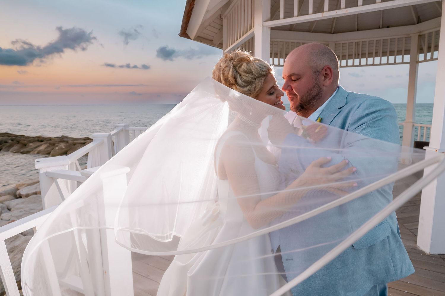 Couple shares romantic moment on beach with flowing veil at sunset.