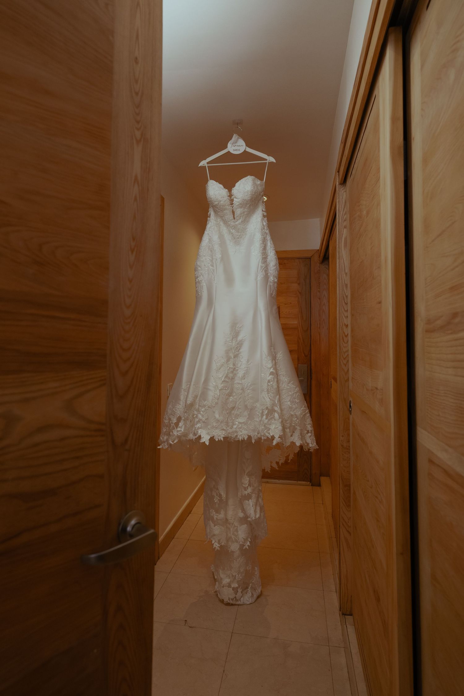 Elegant white lace wedding dress with sweetheart neckline hanging in a wooden hallway.