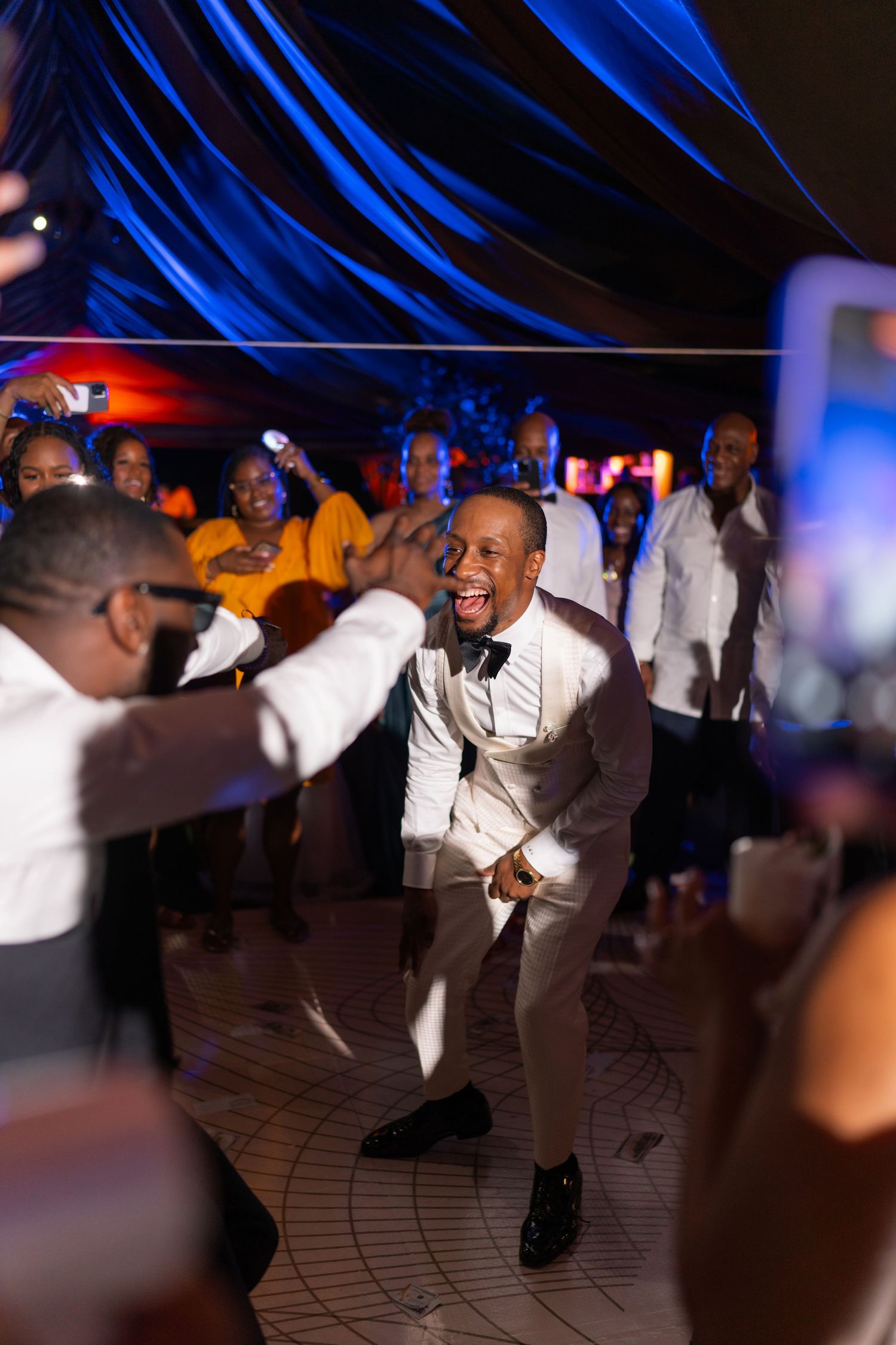 Wedding guests dancing energetically on illuminated dance floor with blue lighting effects.