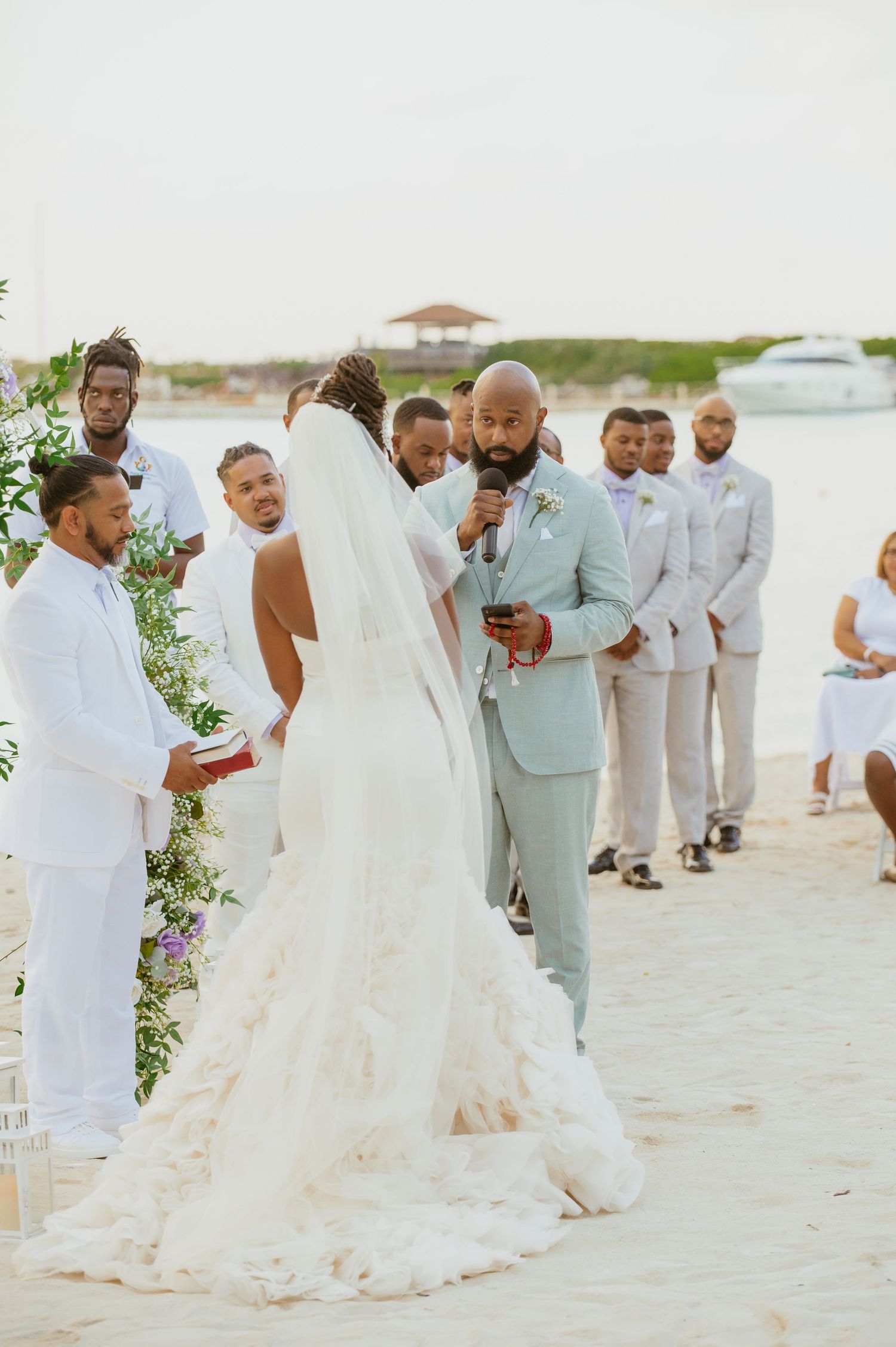Wedding celebration on a sandy beach with guests in white and mint green attire.