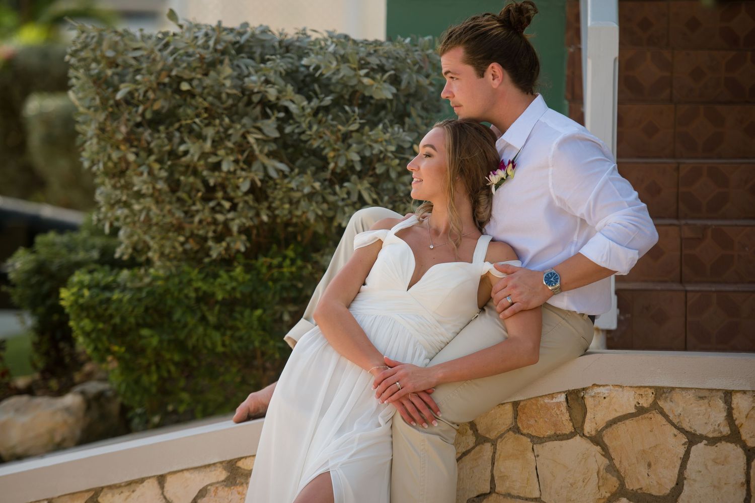 Wedding couple embraces tenderly against natural stone and garden background.