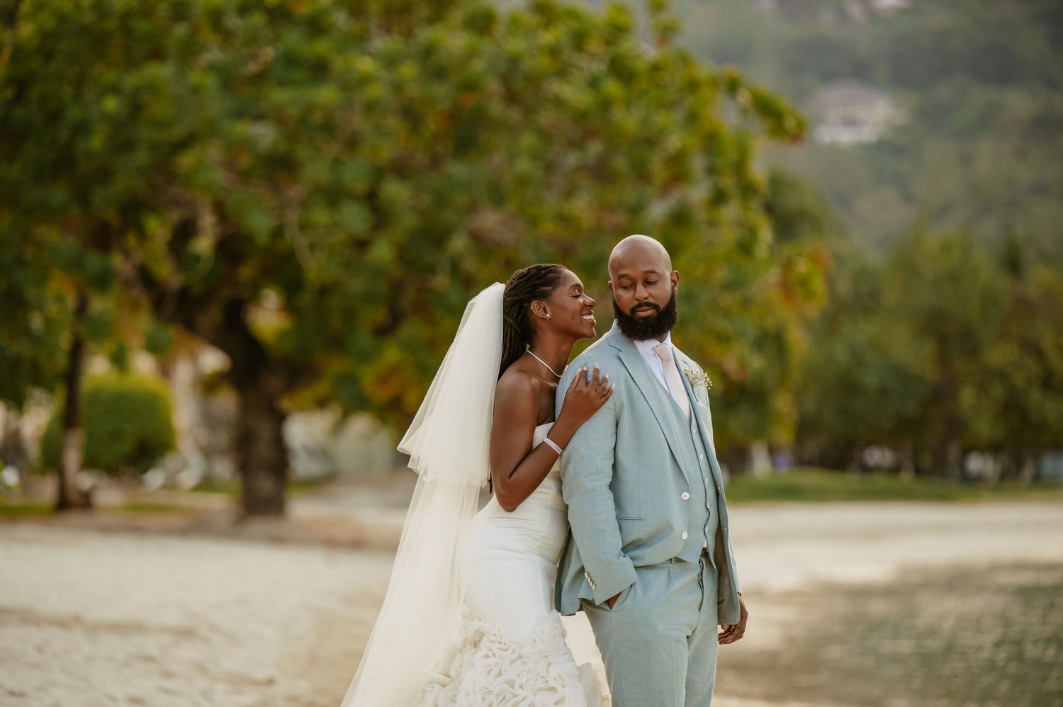 A romantic beach wedding portrait with palm trees and ocean views in the background.