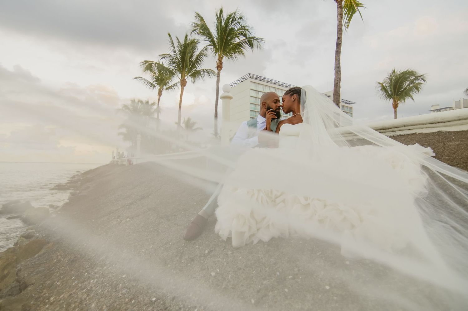 Tropical beach wedding ceremony setup with white chairs and palm trees against a cloudy sky.