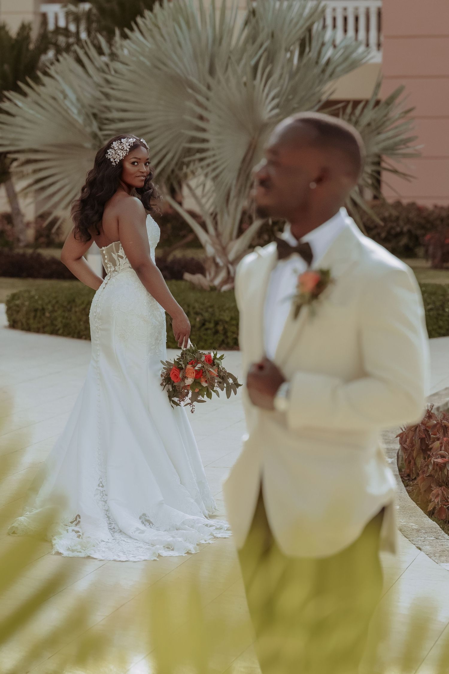 Elegant wedding couple shares an intimate moment in a garden setting with palm trees.