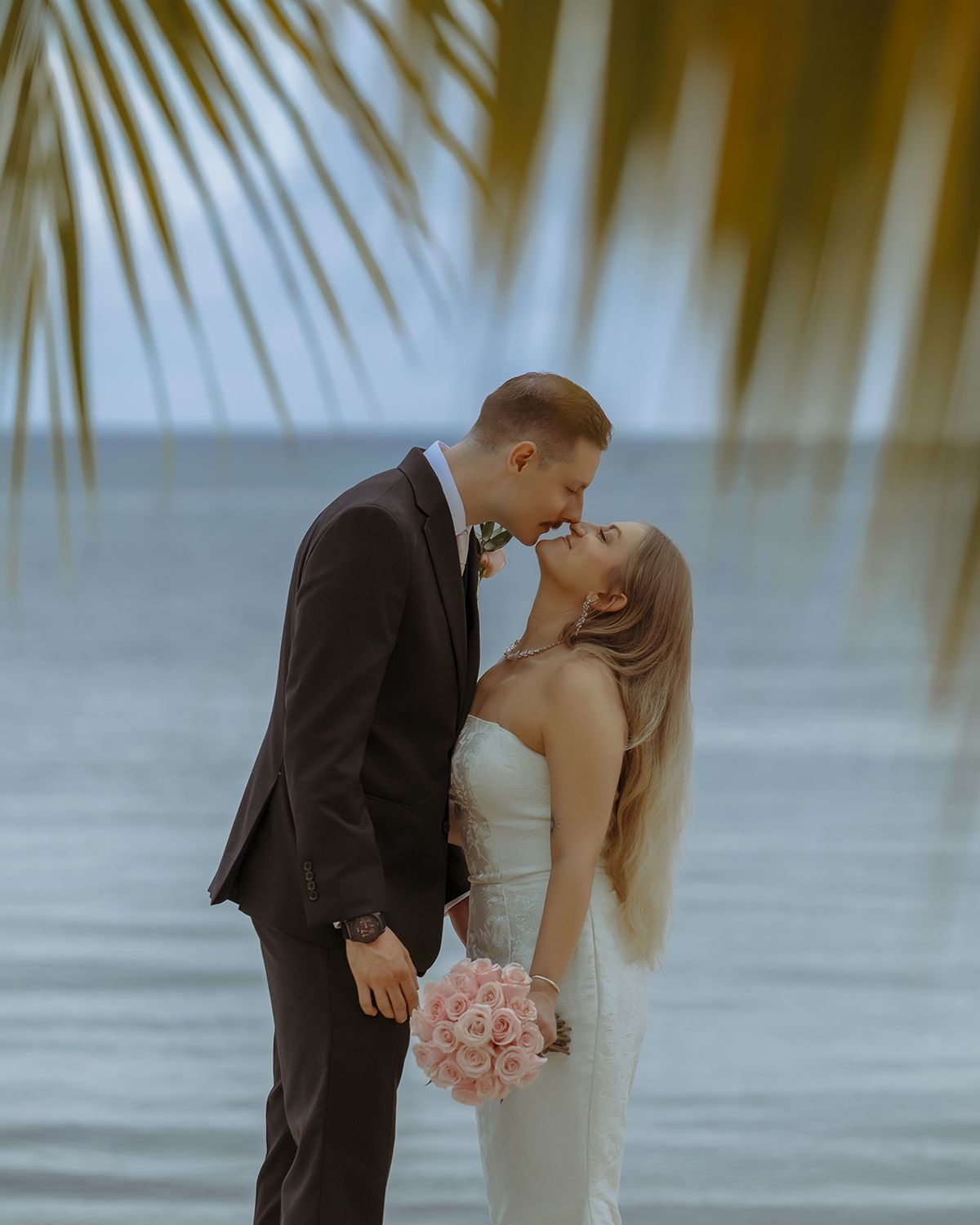 A romantic beachside wedding moment with couple in formal attire against ocean backdrop.