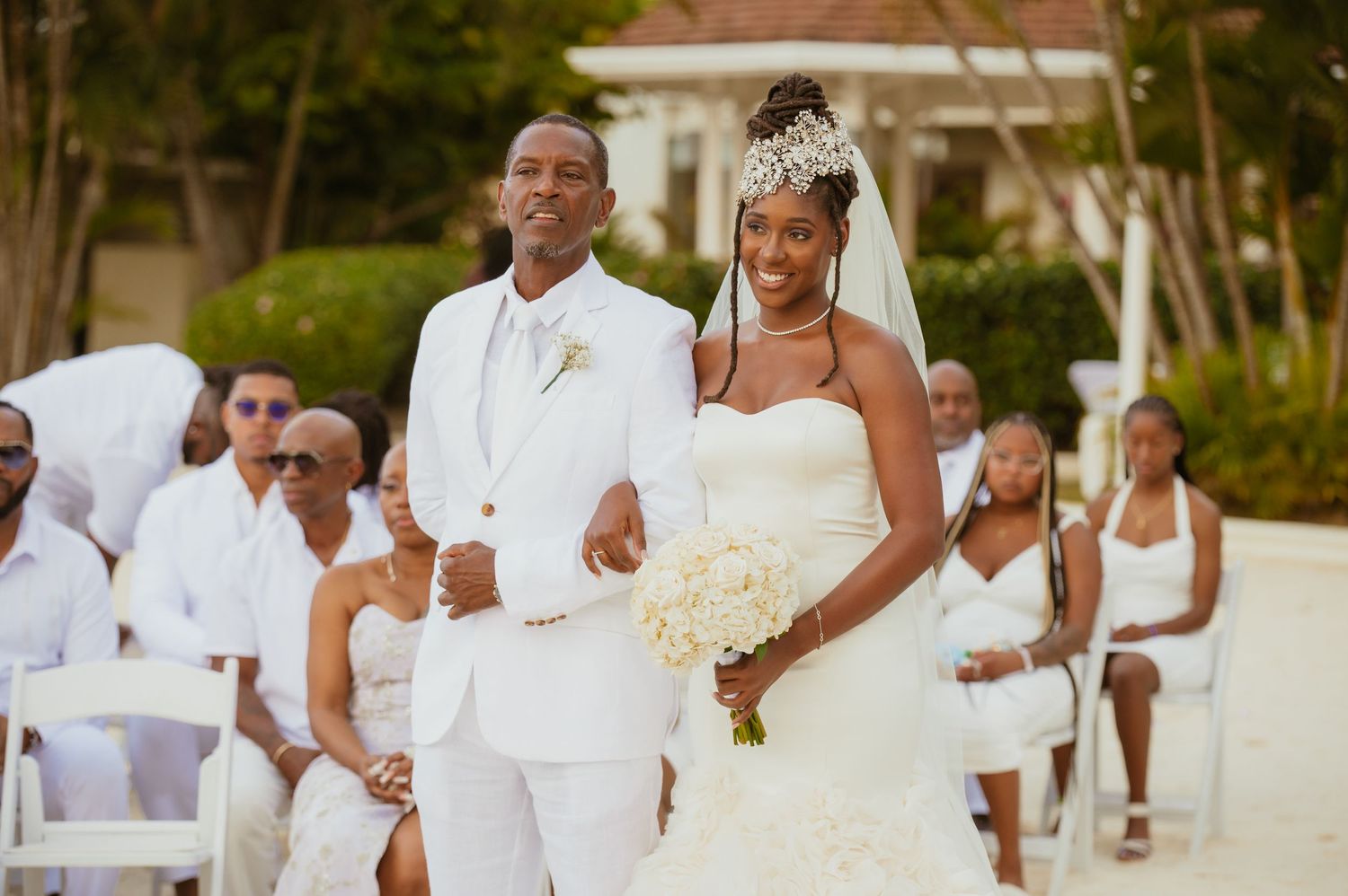 Wedding party in all white attire gathered on a scenic beachfront.