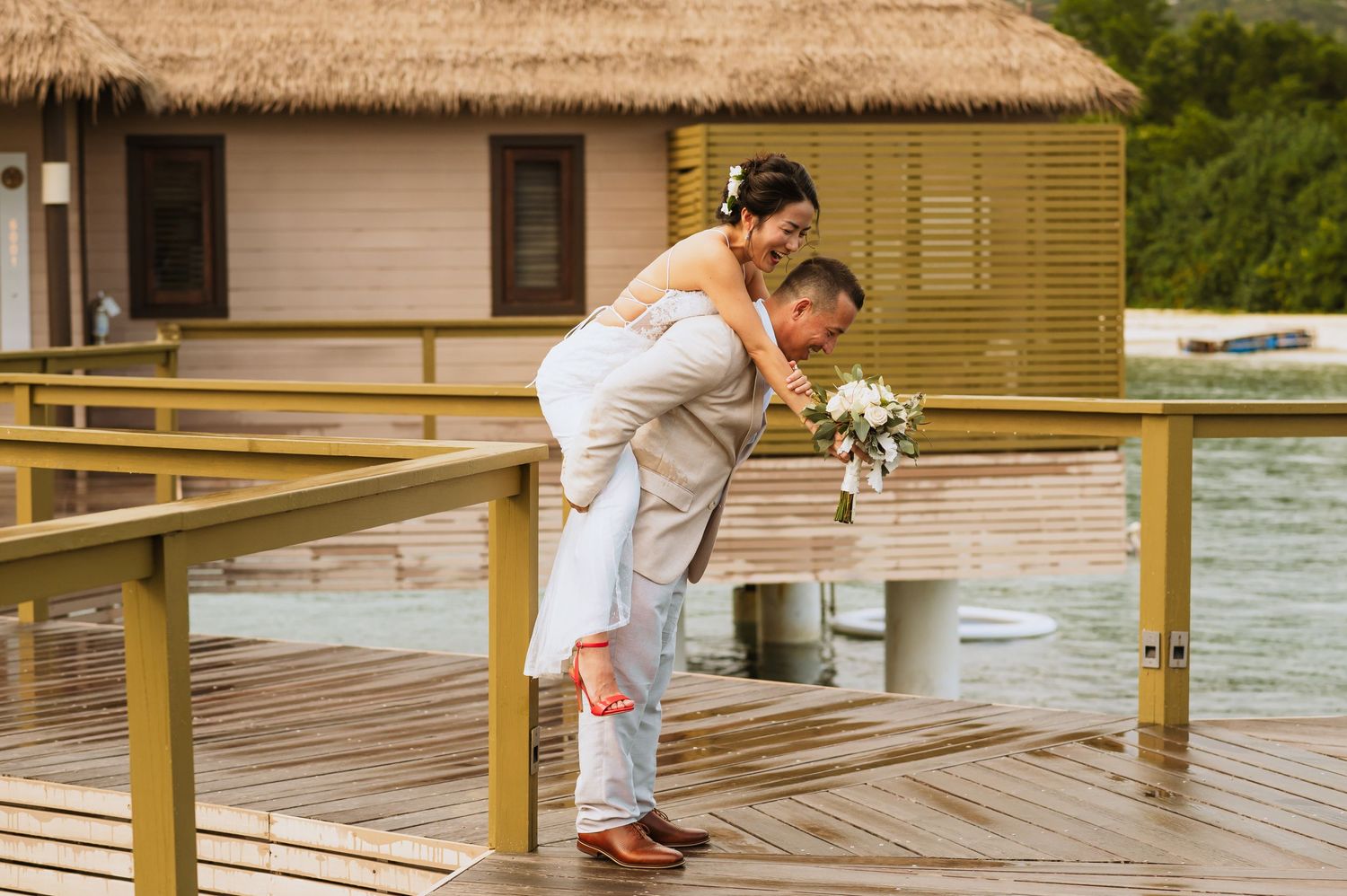 A couple shares a playful moment on a wooden deck over water at an overwater bungalow resort.
