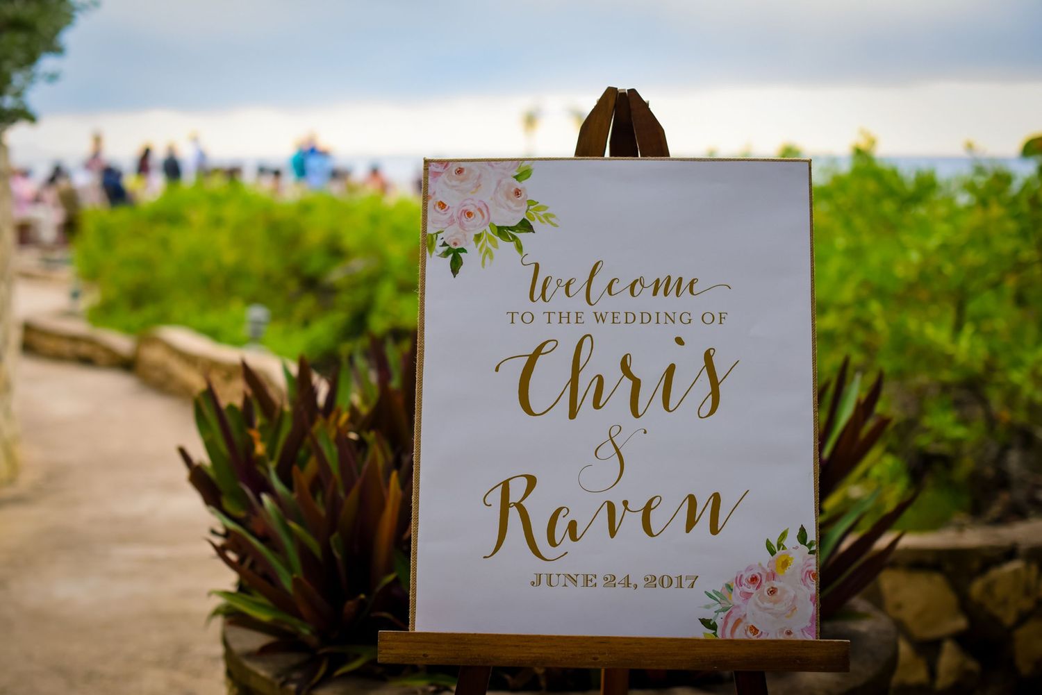 Elegant wedding welcome sign with gold calligraphy for Chris and Raven displayed on an easel outdoors.