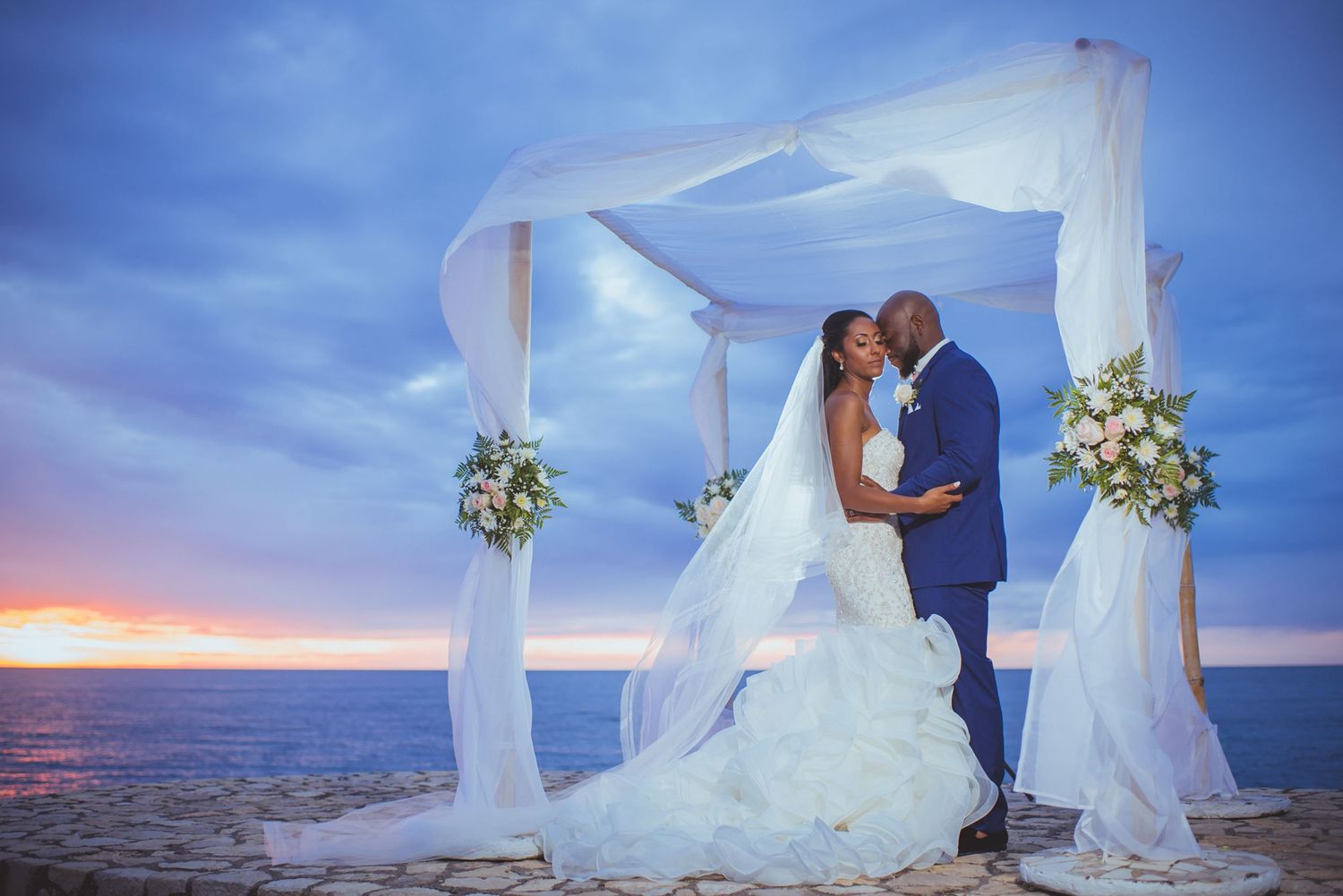 Elegant beach wedding setup with white fabric gazebo and floral arrangements by the ocean.