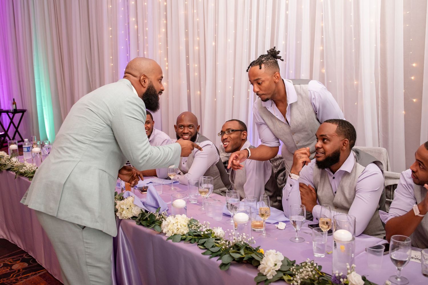Wedding party socializing at decorated head table during reception celebration.