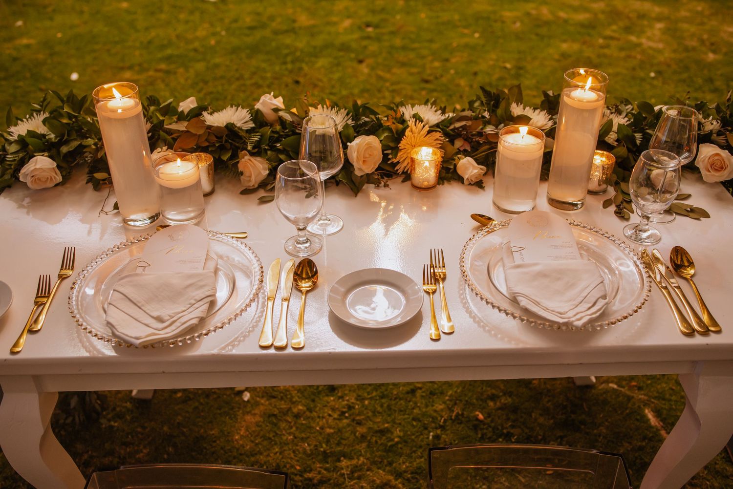 Luxurious table setting with white candles, elegant dinnerware and romantic floral arrangements.