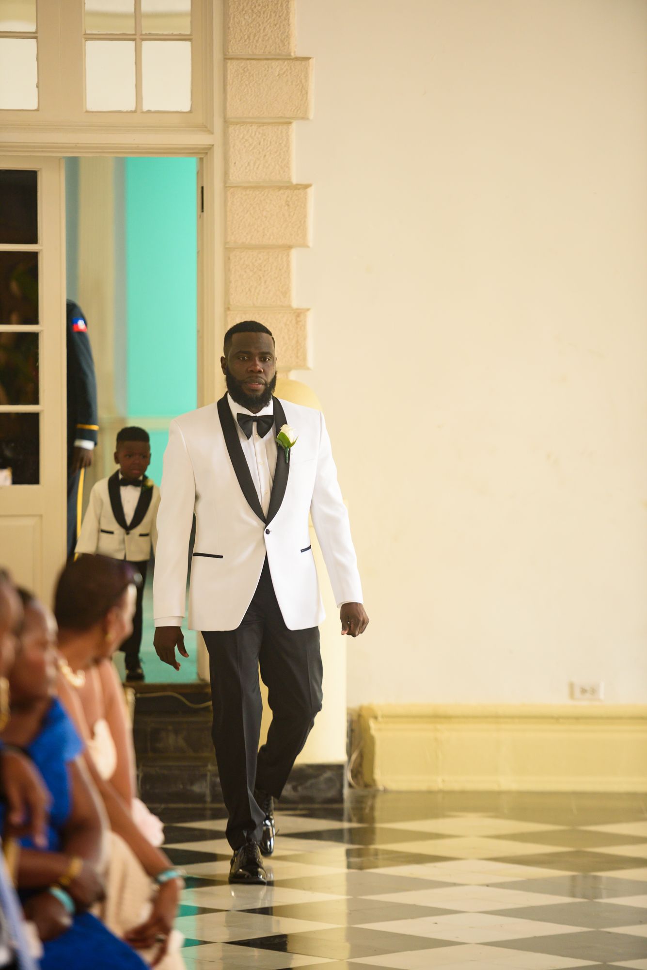 Wedding party members in formal attire walking across a black and white checkered floor.