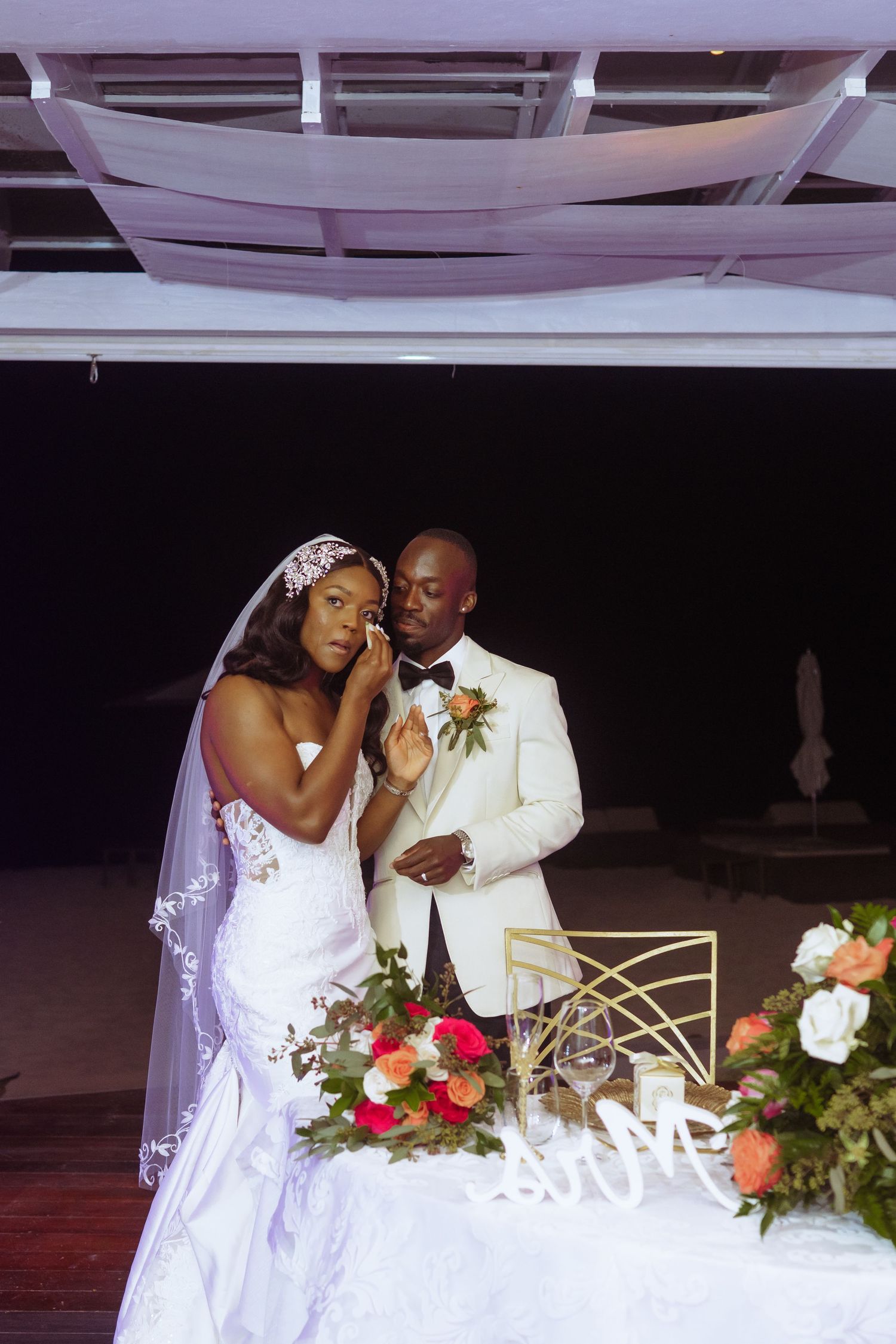 Wedding couple sharing intimate moment at reception with decorative lighting and floral arrangements.