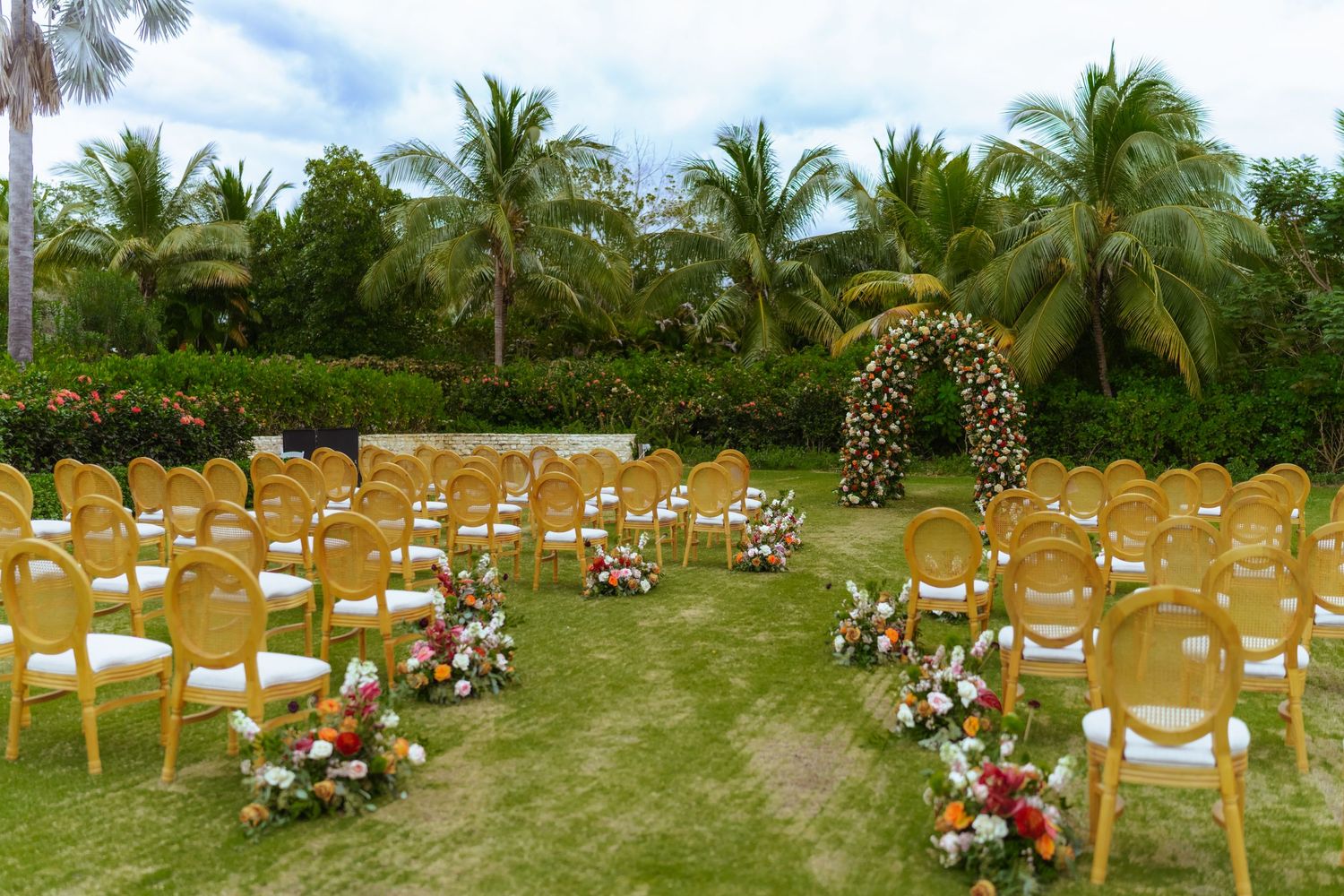 Panoramic view of a tropical garden wedding venue with rows of golden chairs and floral decorations.