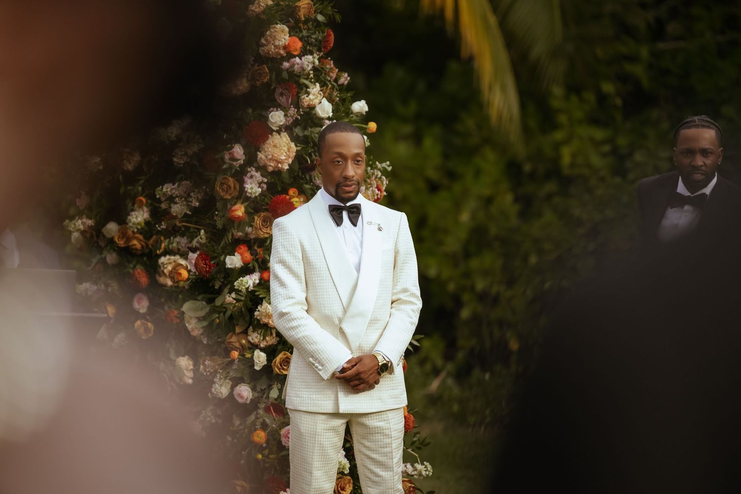Outdoor wedding ceremony with white and coral floral arrangements under palm trees.