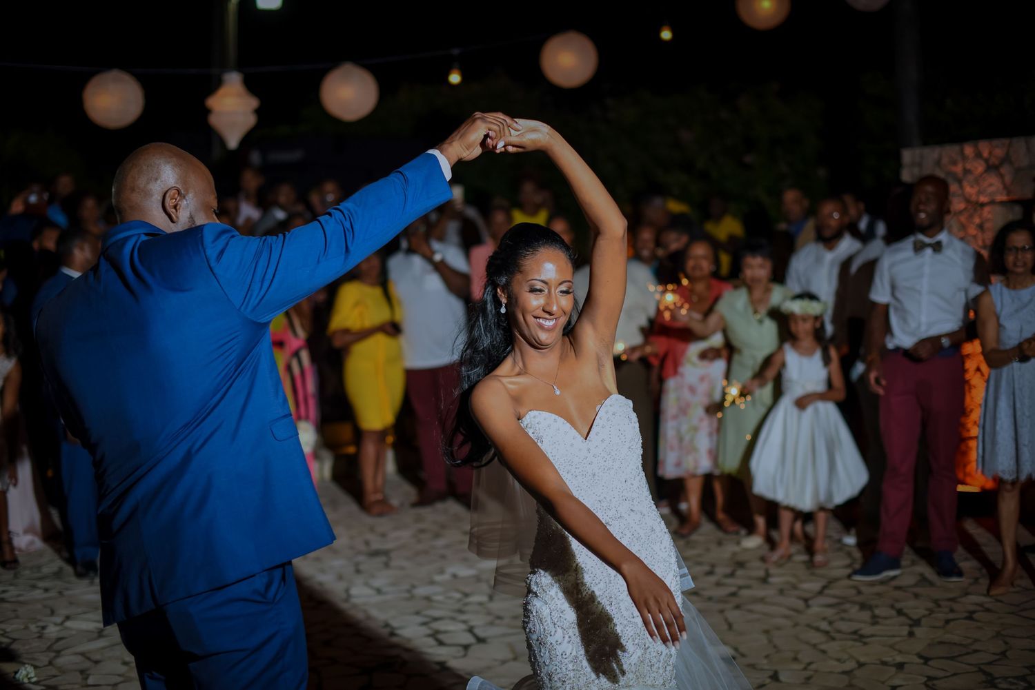 Wedding guests dance and celebrate on a sandy beach during an evening reception.