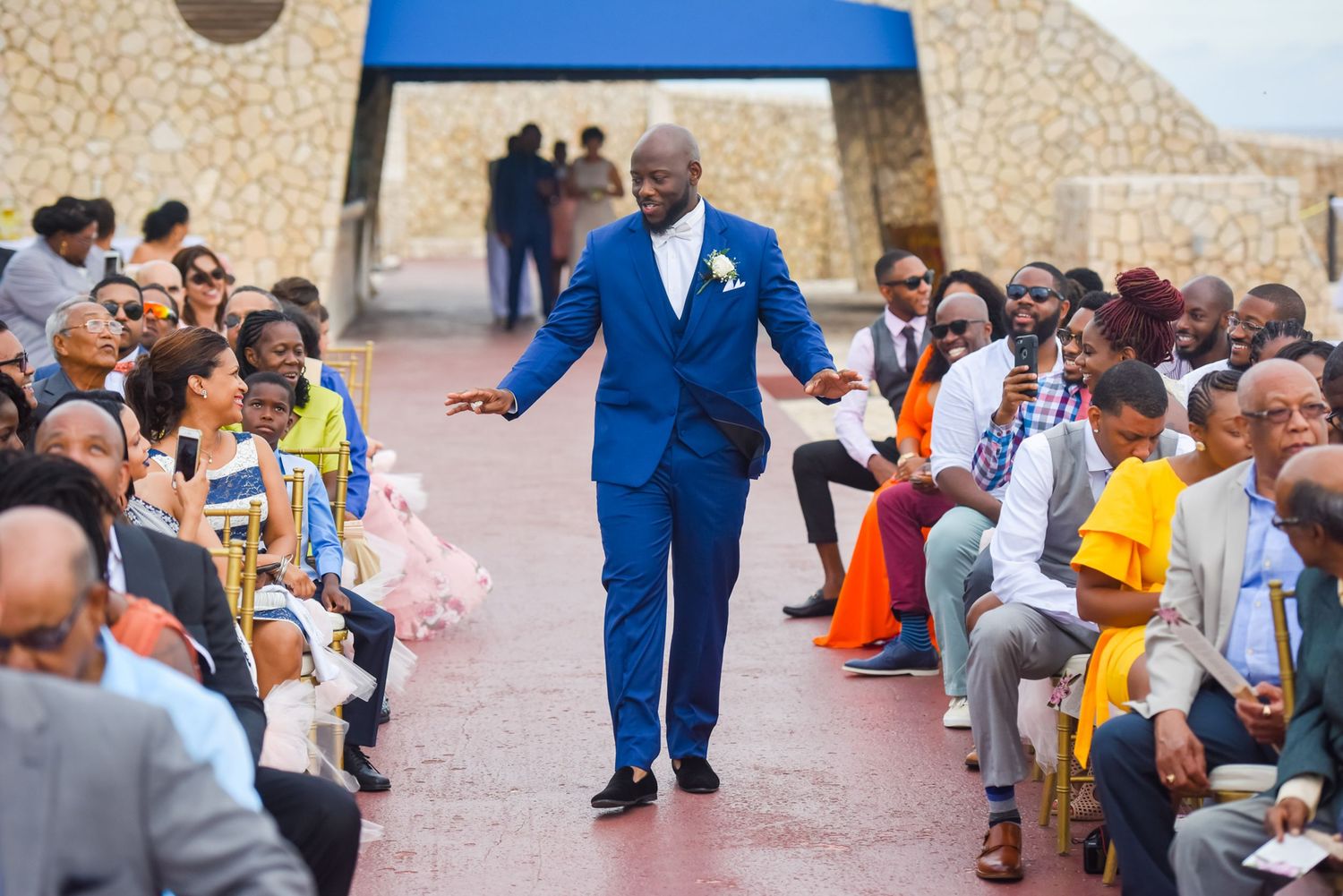 Wedding processional with attendee in bright blue suit walking down aisle between seated guests.
