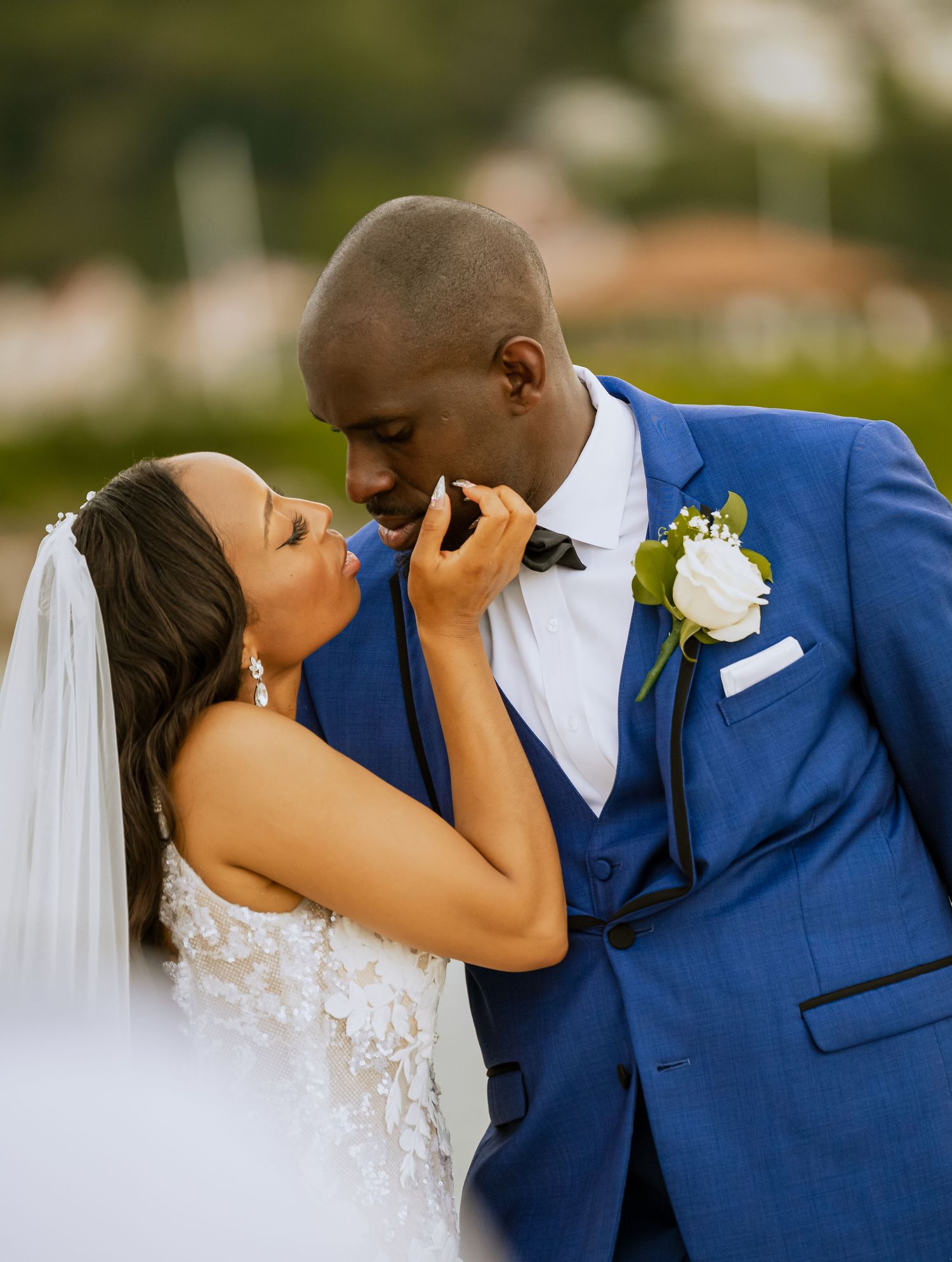 Romantic wedding couple in blue suit and white dress share intimate kisses in a beautiful outdoor setting.