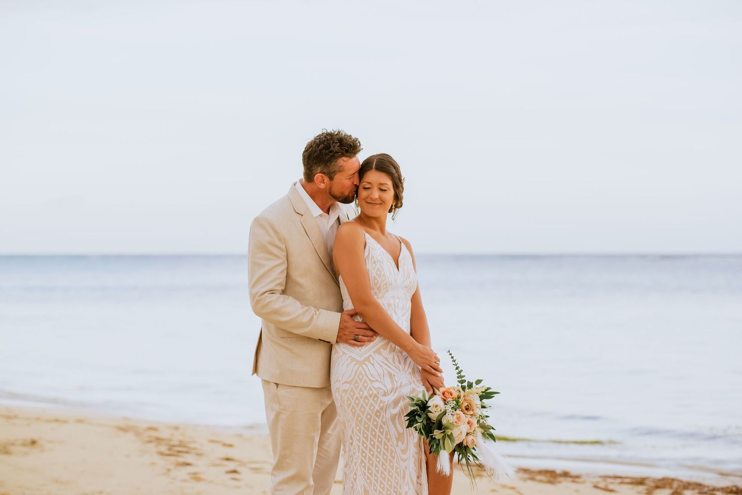 A romantic couple embraces on a serene beach during sunset for their wedding photos.