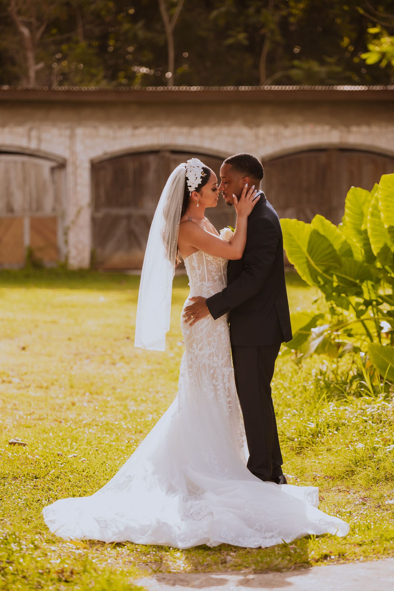 Newlyweds share an intimate moment in a garden setting with a stone wall backdrop.