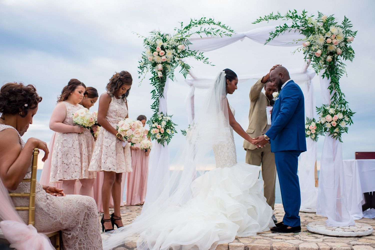 Wedding party and guests gathered under elegant white tent with floral decorations.