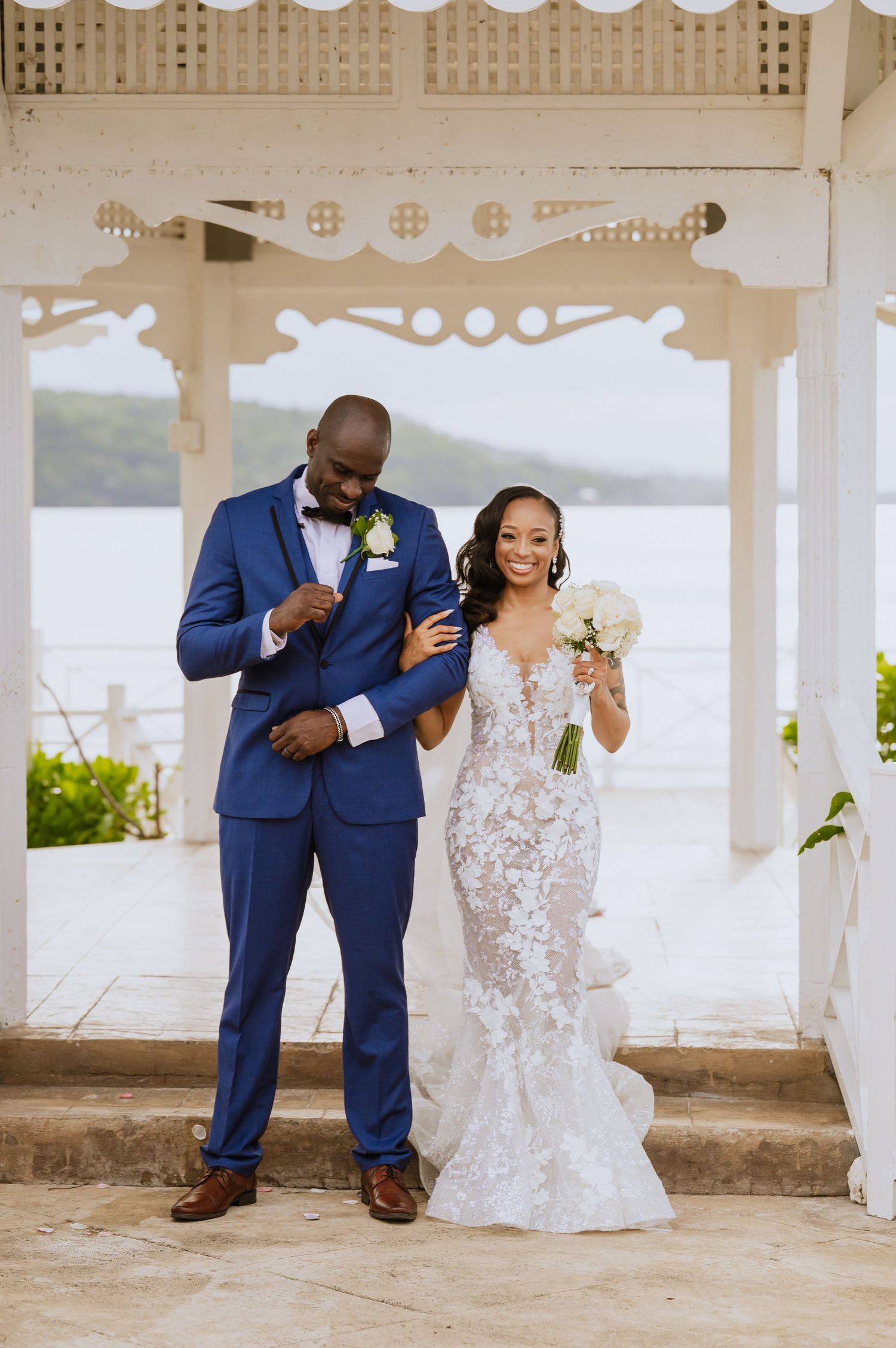 Happy newlyweds celebrate in an ornate white gazebo by the water.
