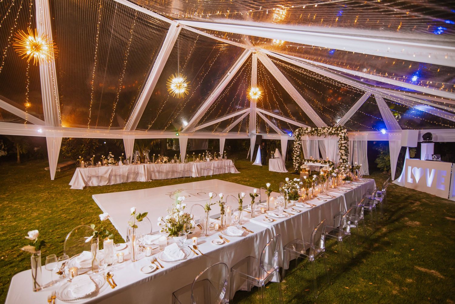 Elegant outdoor wedding reception under clear tent with long tables and romantic lighting.
