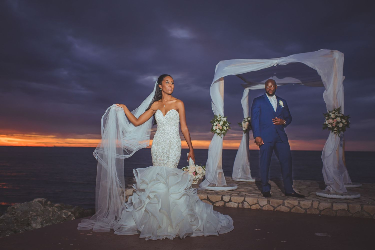 Seaside wedding venue with elegant white draping and floral decor against blue sky.