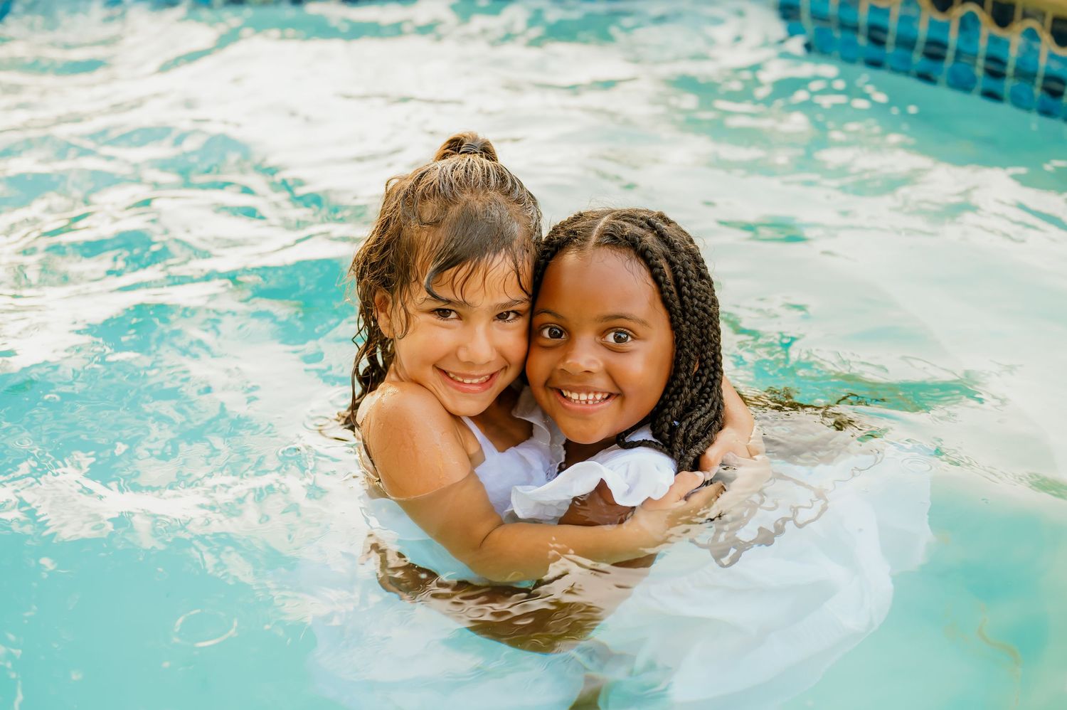 Two children embrace while swimming and playing in a bright blue pool.