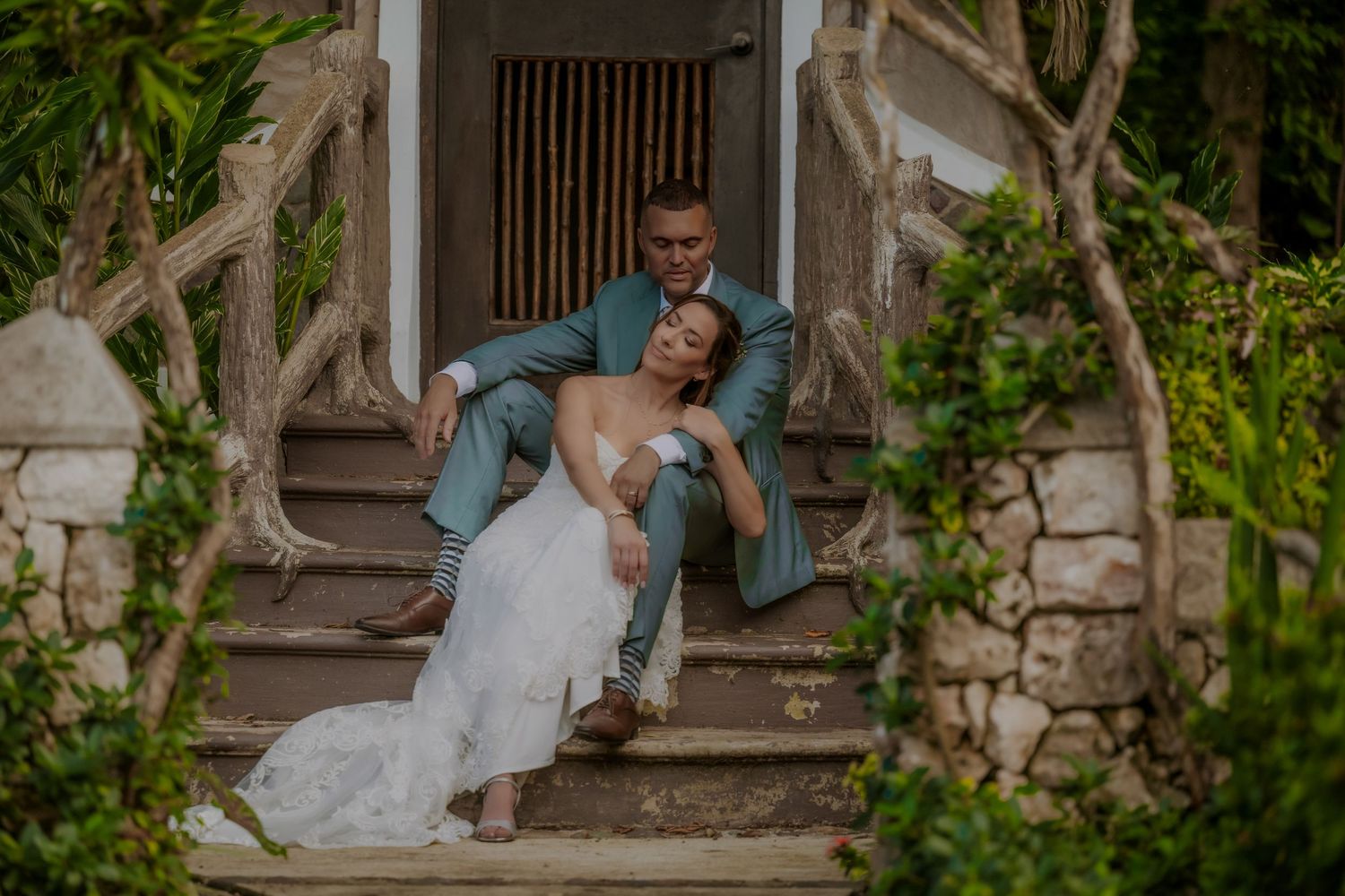 A couple in wedding attire shares romantic moments on rustic stone steps surrounded by lush greenery.