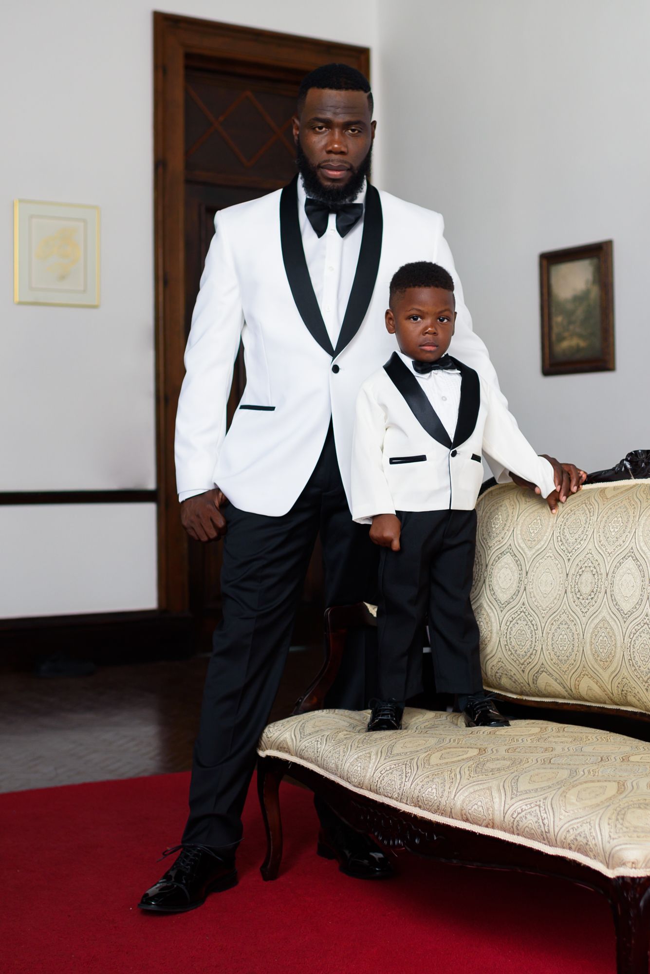 Two people in white tuxedo jackets sitting on an elegant beige couch.