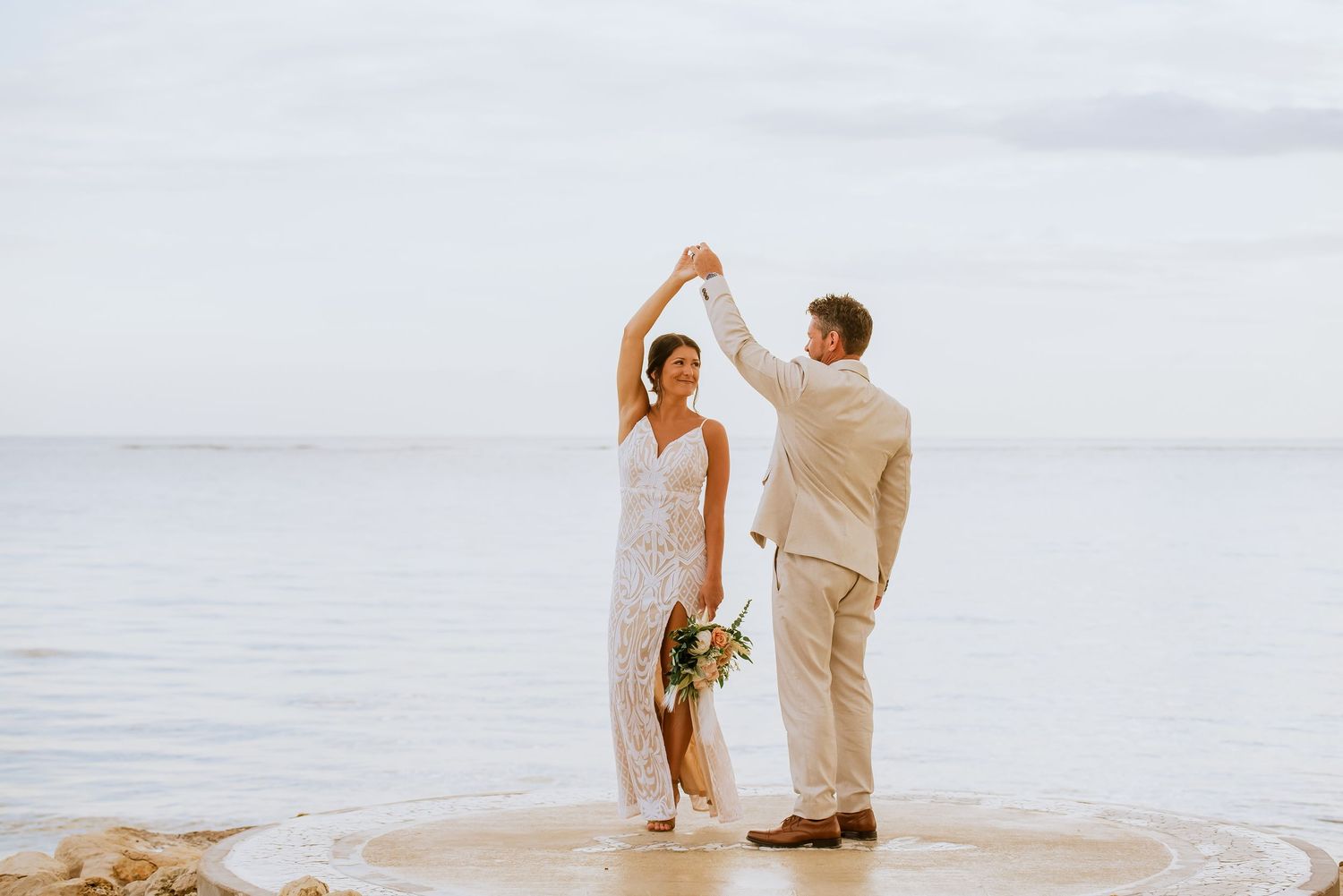 Couple performs romantic dance moves on a round concrete platform by the sea.