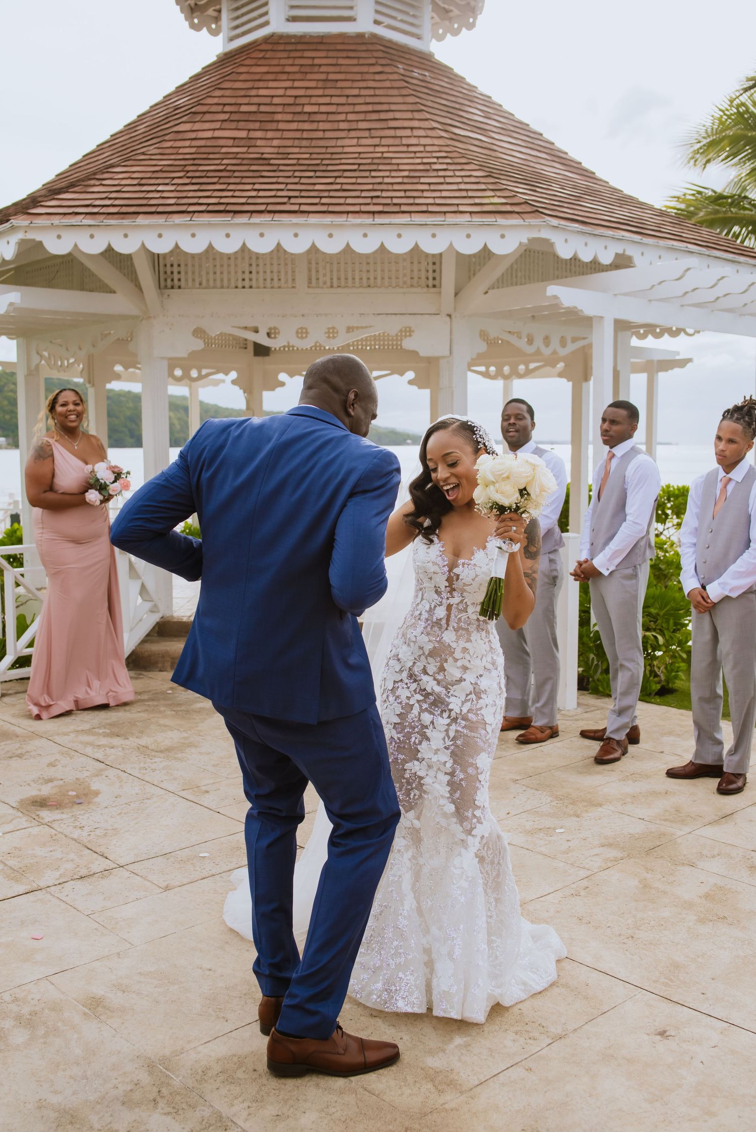 A joyful wedding ceremony takes place under an elegant white gazebo by the ocean.