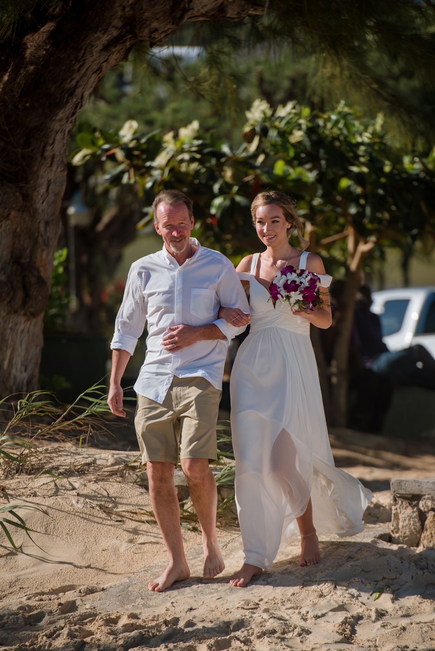 Couple walking barefoot together on a sandy beach during their casual beach wedding celebration.