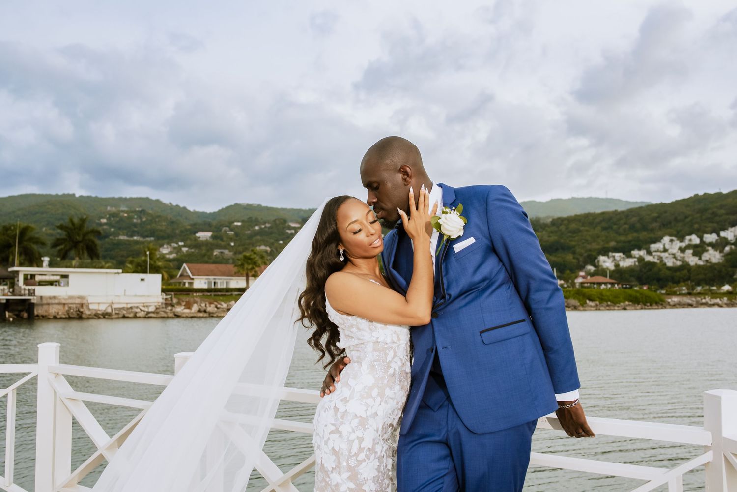 Wedding couple poses on a waterfront deck with scenic mountain and ocean views.