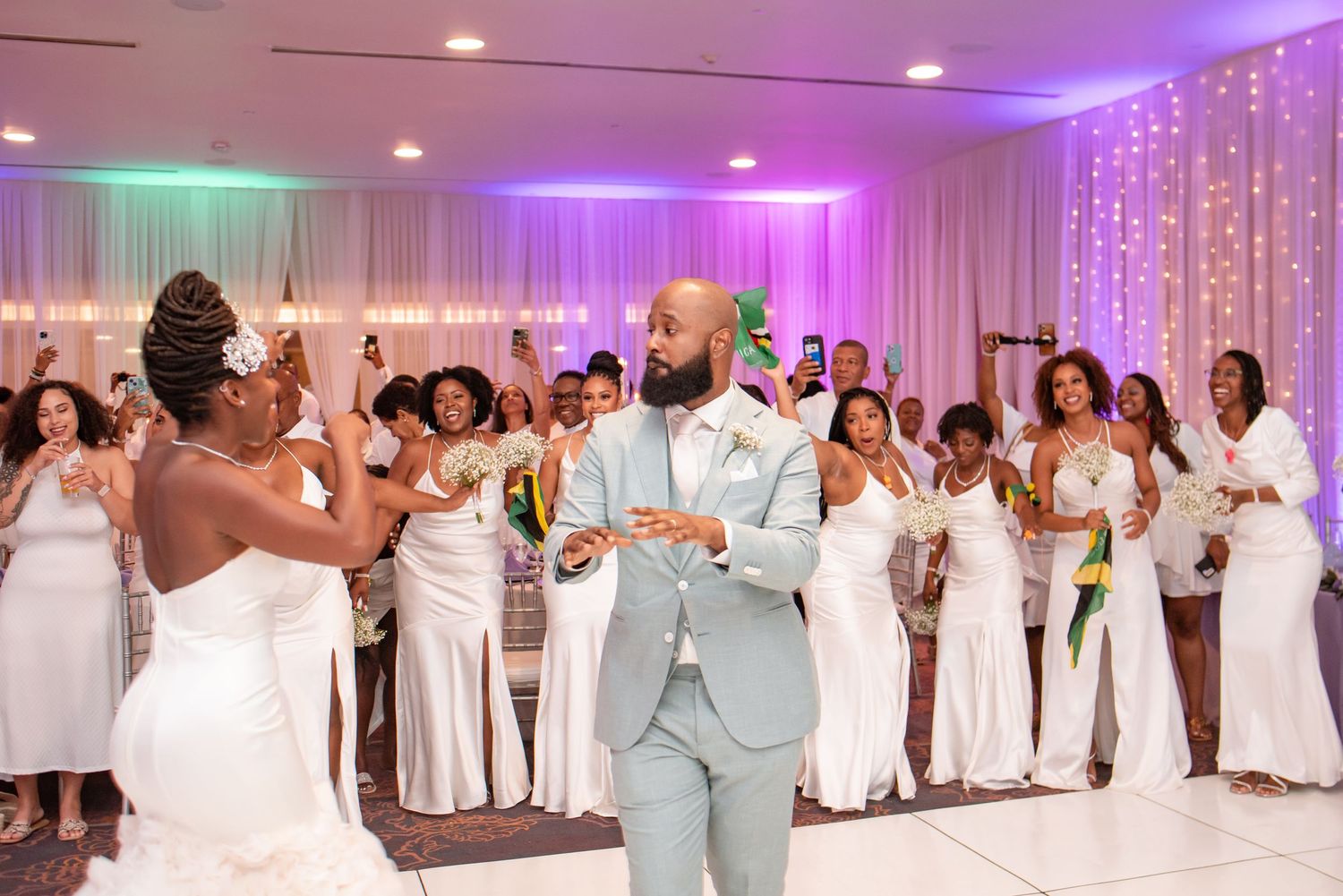 Wedding party dancing and celebrating in a reception hall with purple and teal lighting.