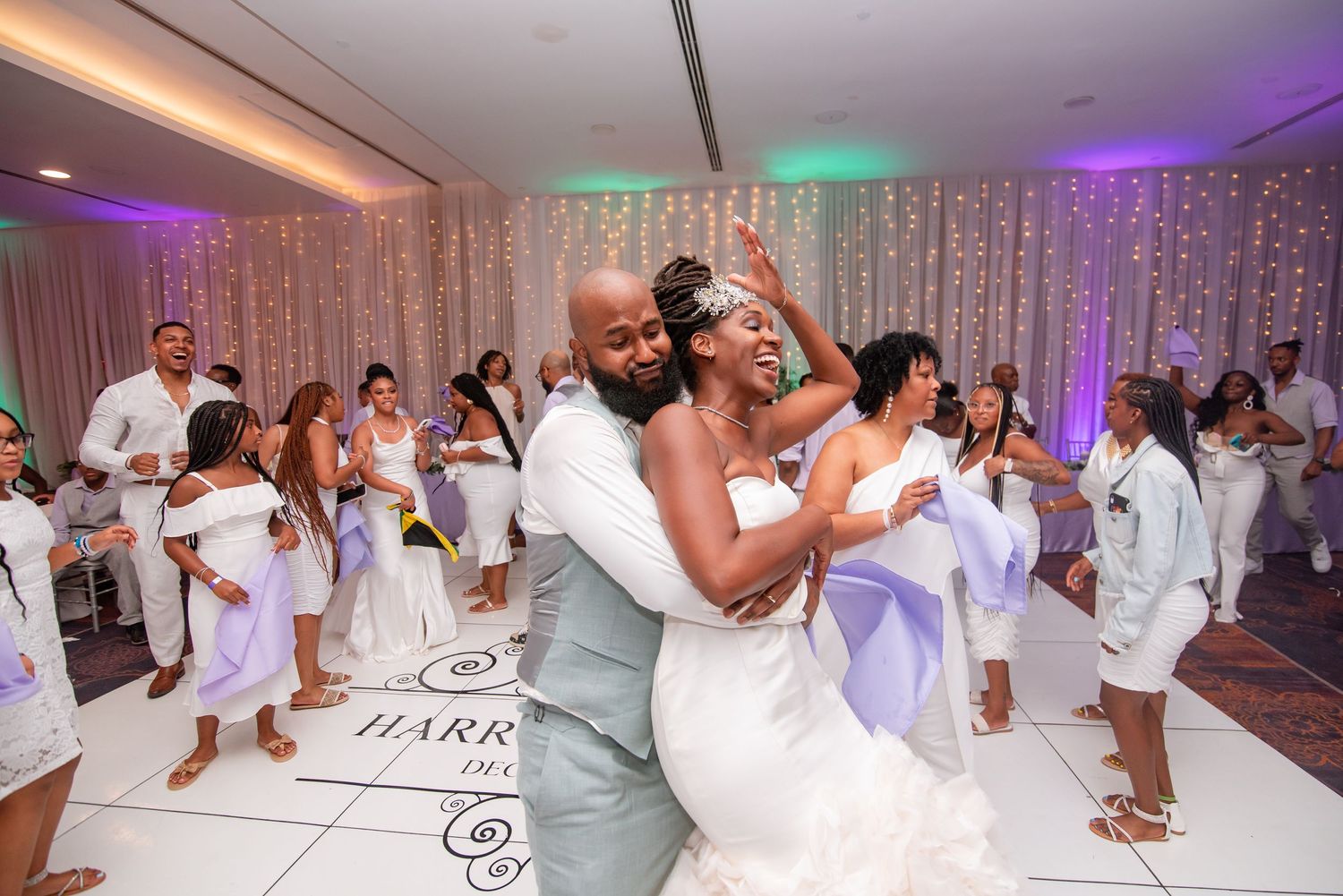 A couple shares their first dance at a wedding reception with white and purple lighting decor.
