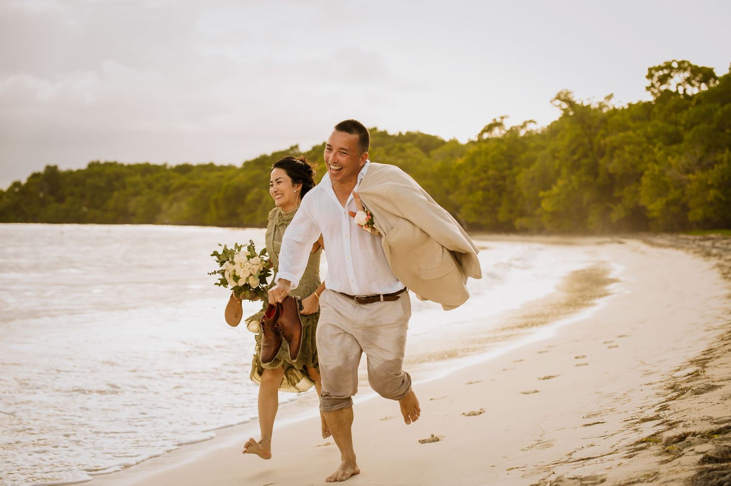 Couple running joyfully along beach shore at sunset.