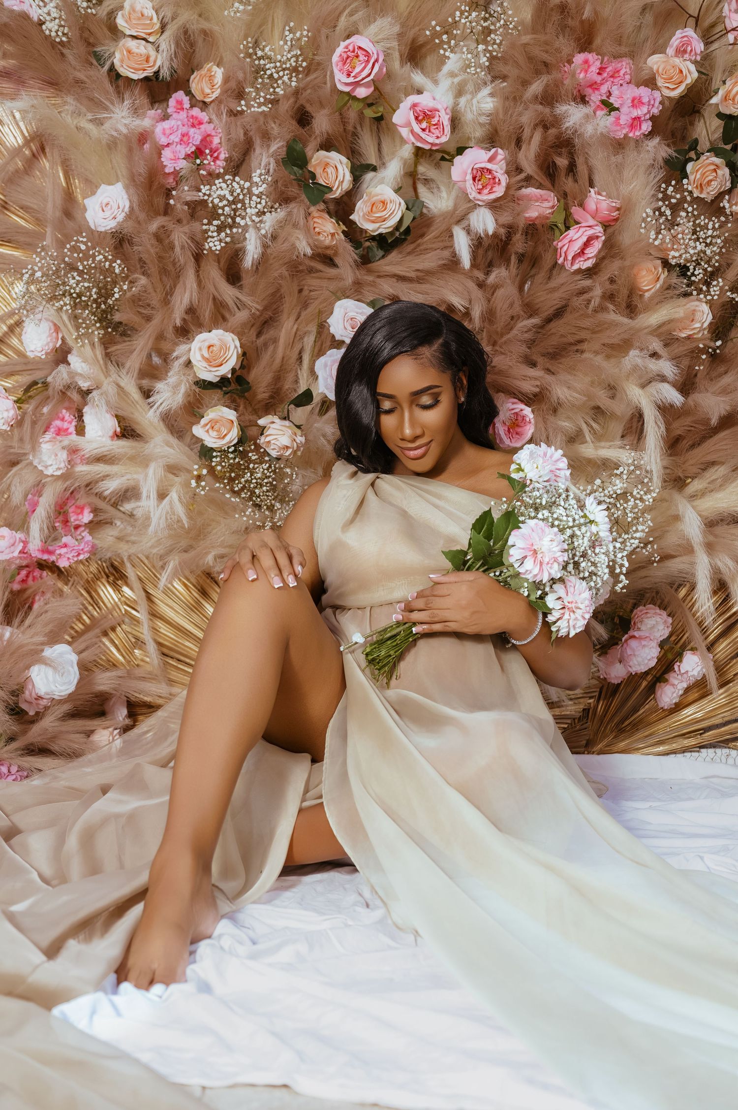 Elegant maternity portrait with pink floral backdrop and white flowing gown.