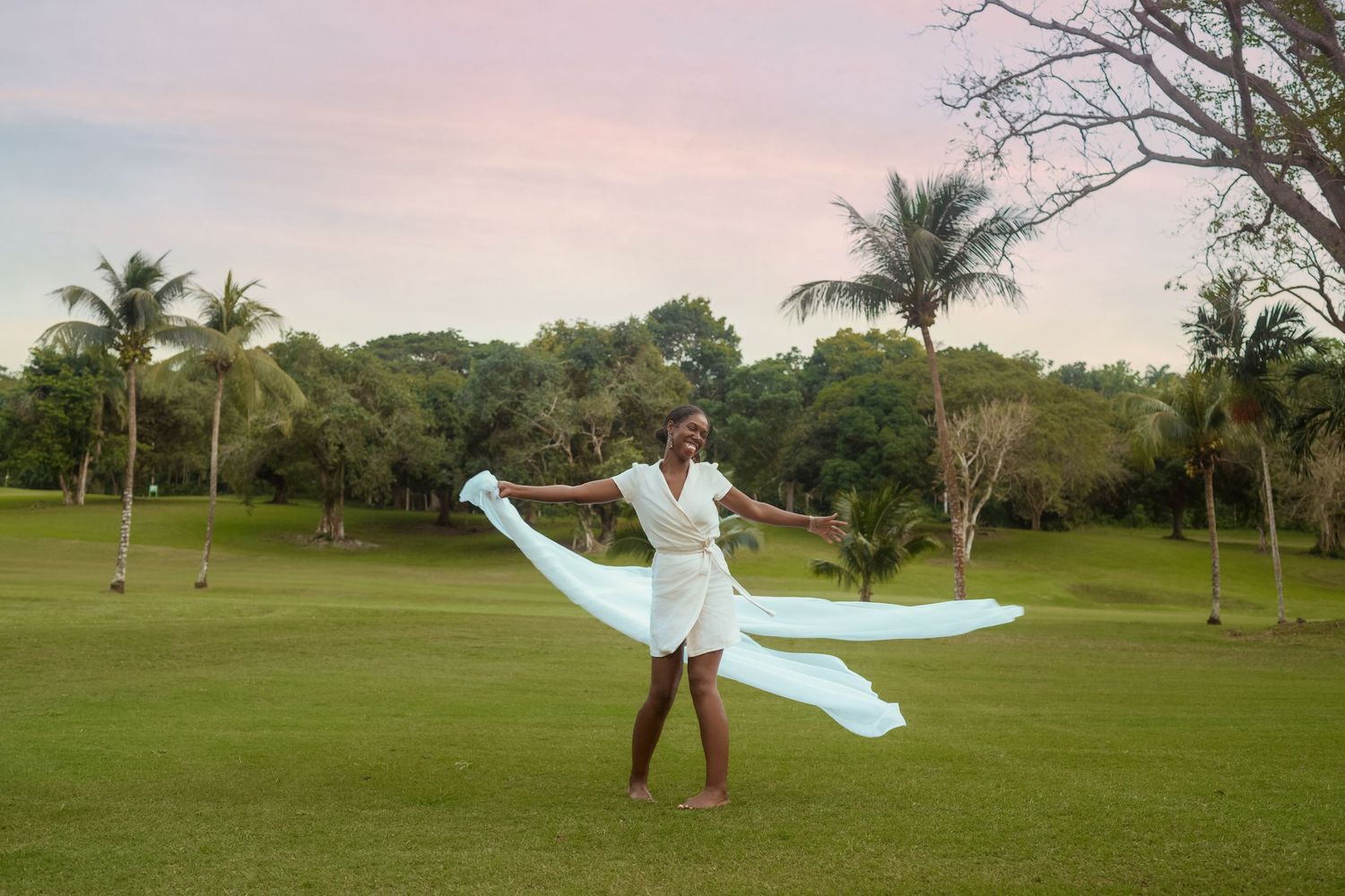 Flowing light blue fabric creates movement against a tropical landscape with palm trees at sunset.