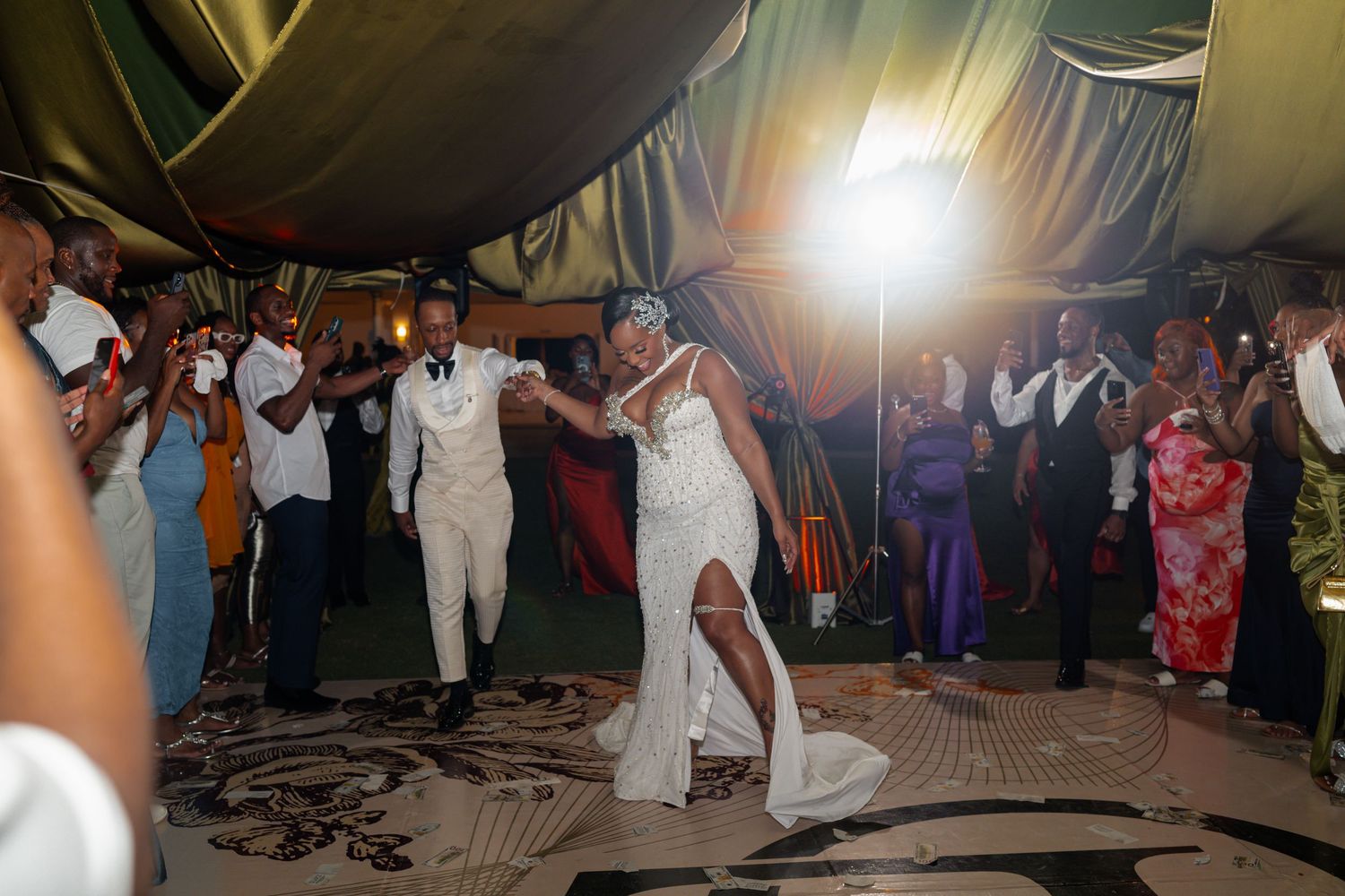 Wedding reception dance floor filled with celebrating guests under tent lighting.