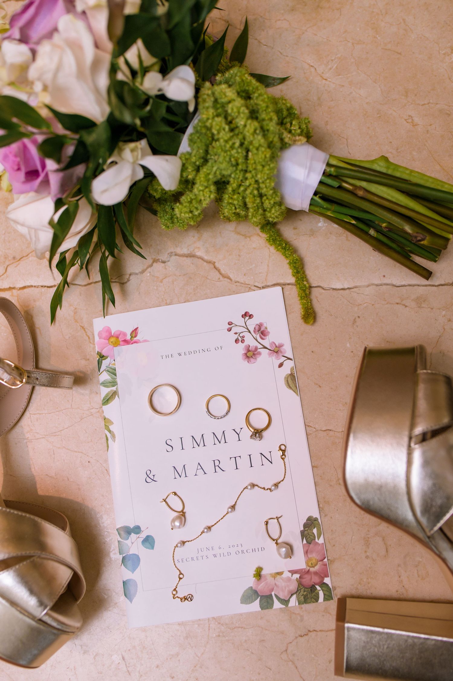 Wedding stationery and rings displayed with pink and green floral arrangements.