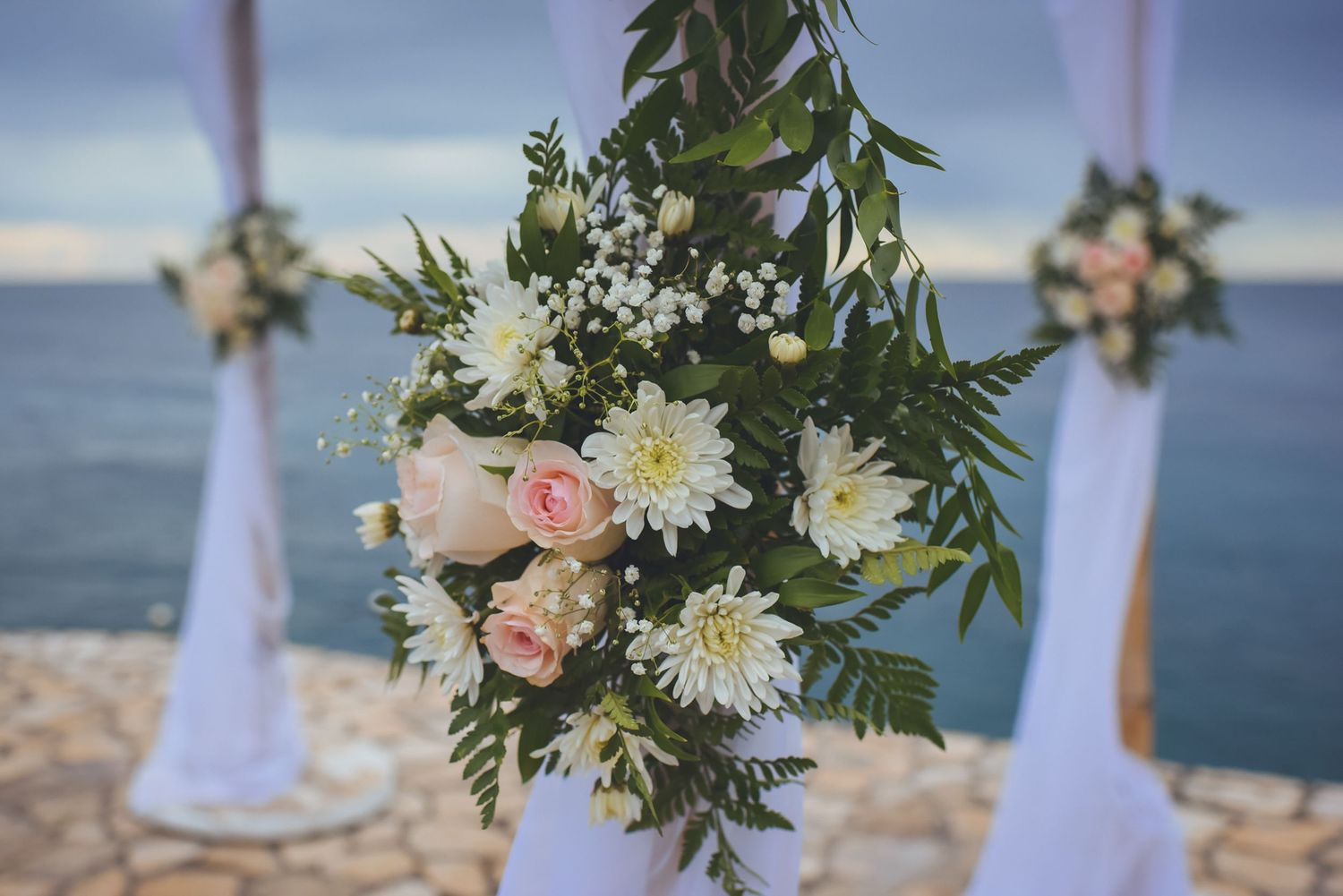 White fabric draped archway adorned with fresh flowers for beach wedding ceremony.