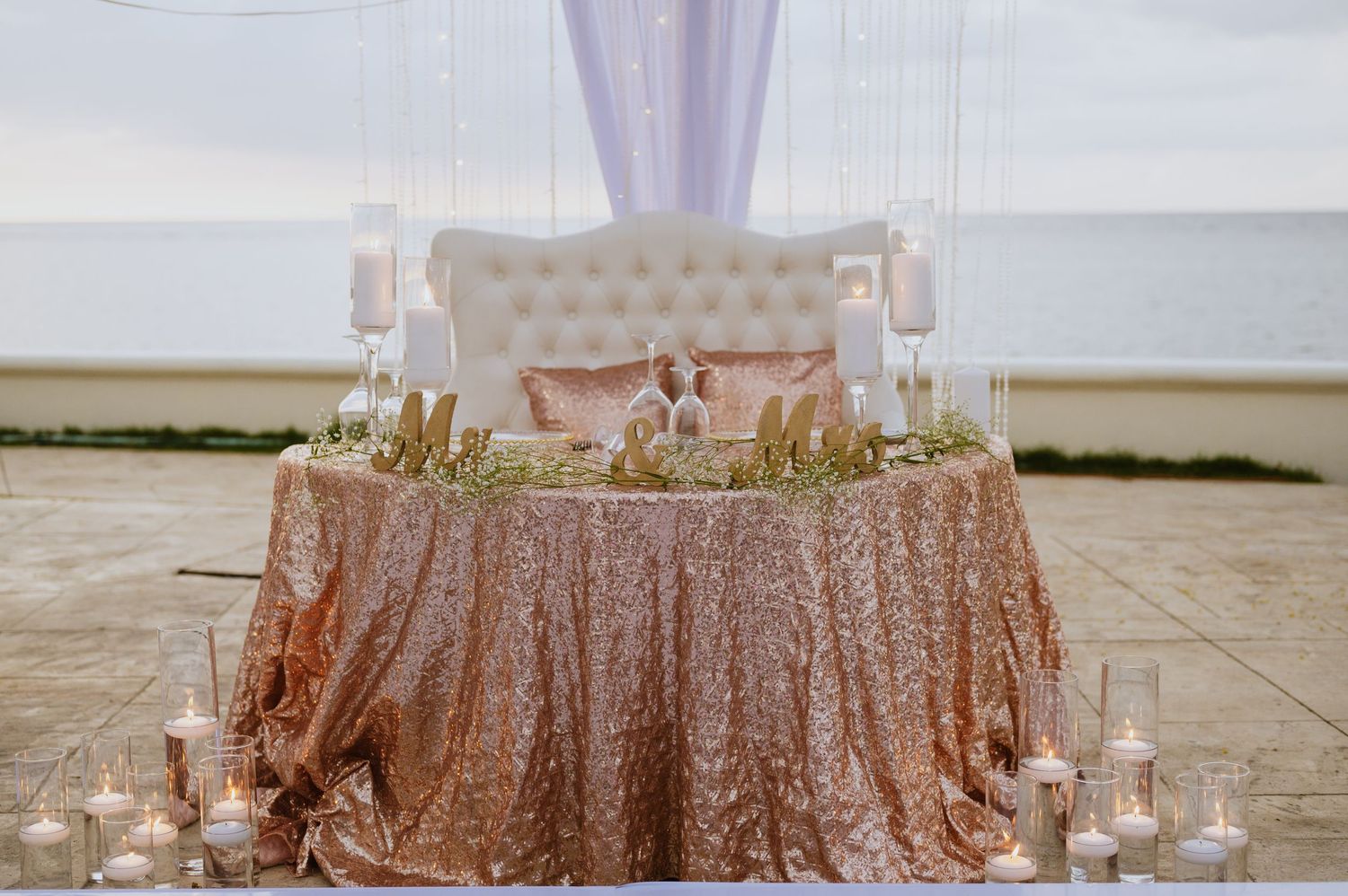 Luxurious sweetheart table with rose gold sequin tablecloth and tufted white throne chairs.