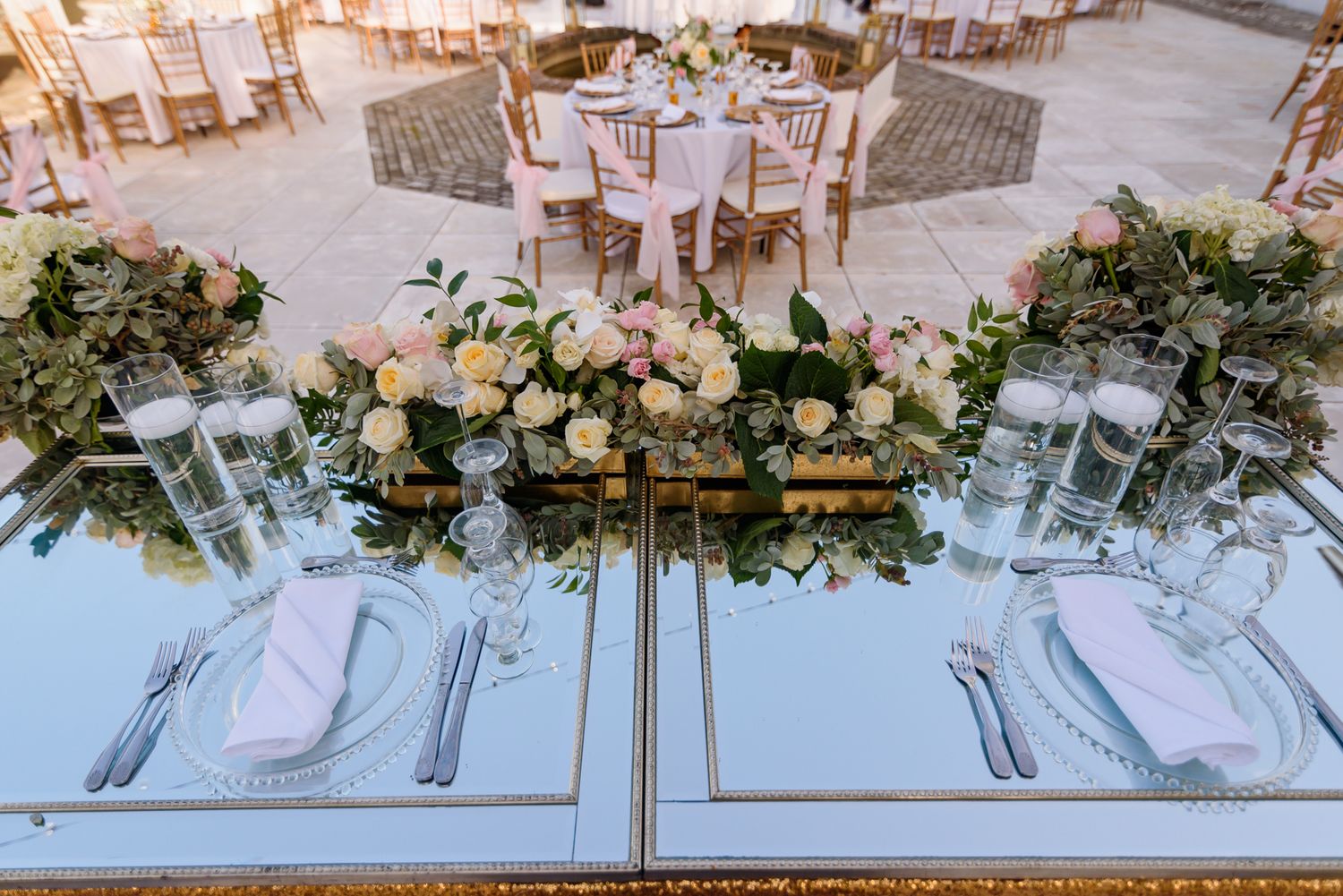 Long wedding reception tables decorated with white linens and greenery garlands.