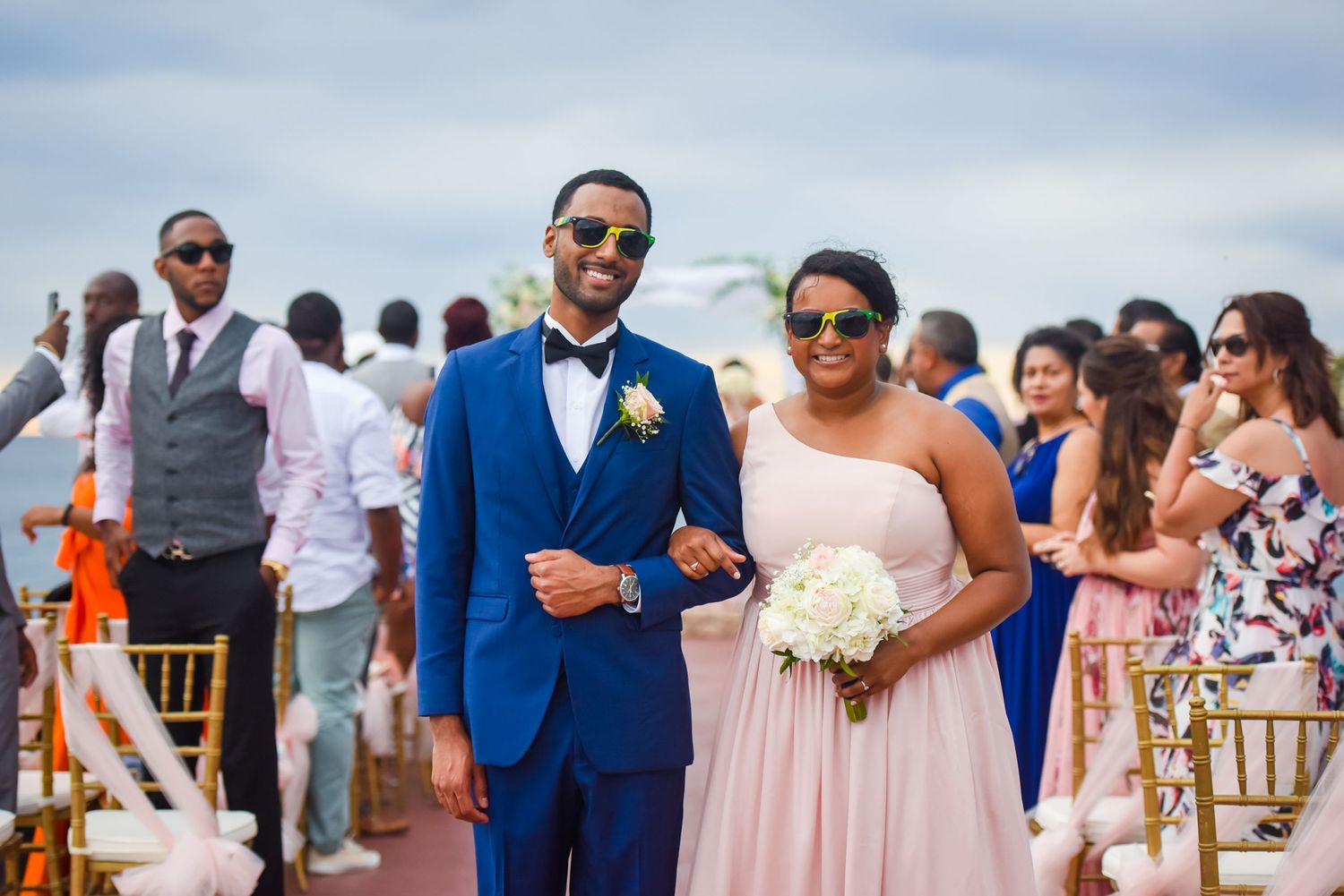 Wedding party members in formal attire gathered at sunny beach celebration.