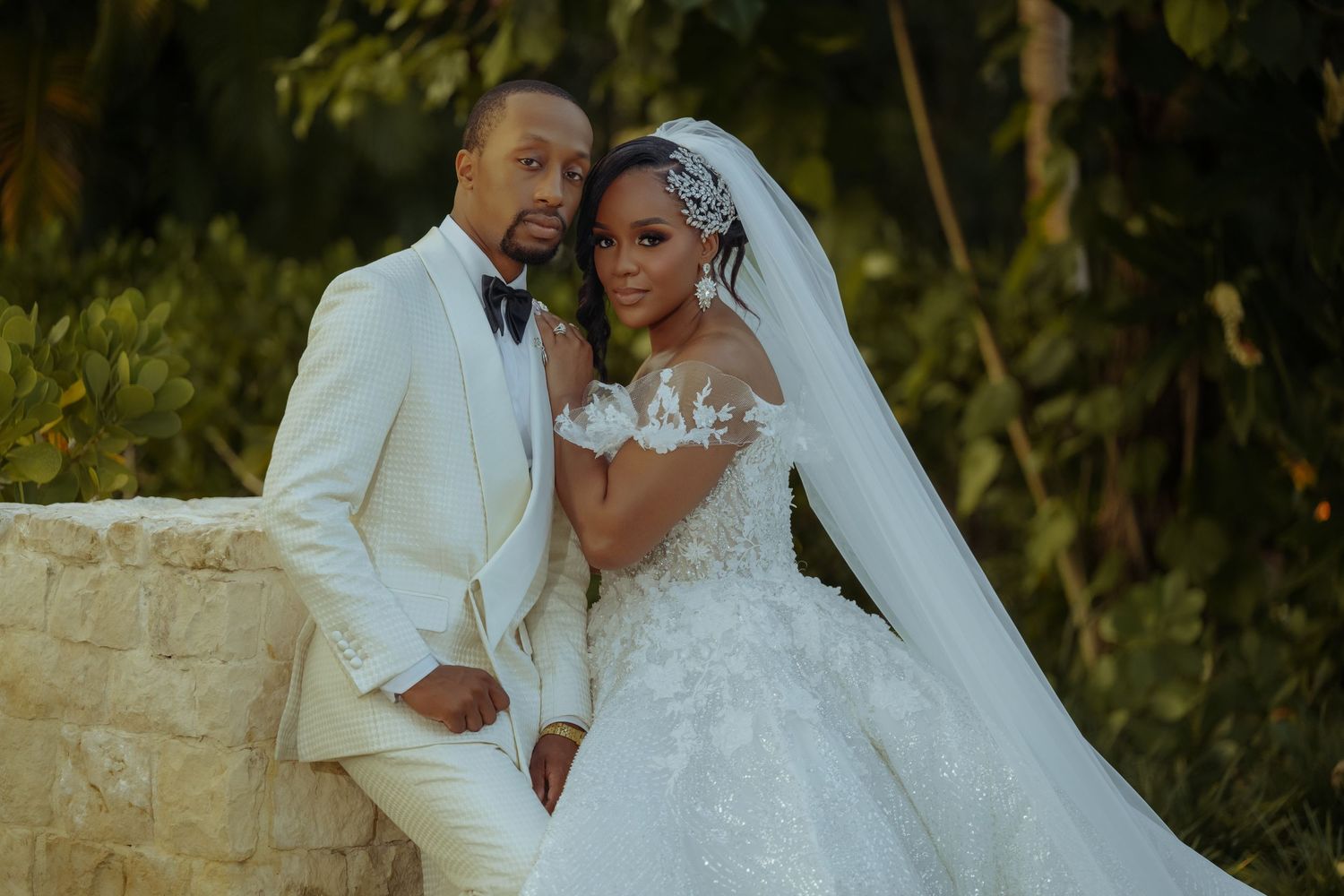 Romantic wedding portraits in a lush garden setting with stone wall backdrop.