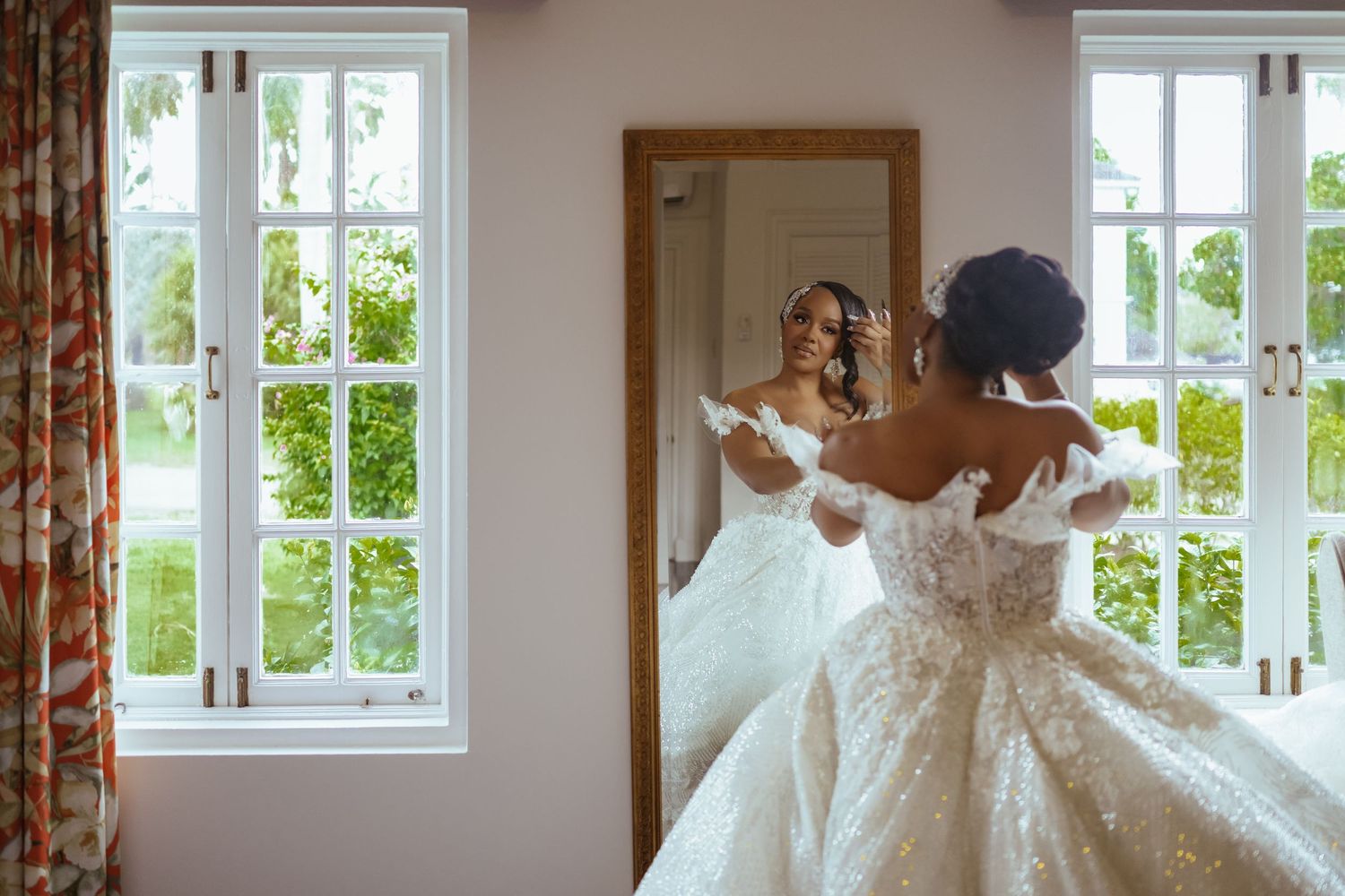 A beautiful white lace wedding dress displayed near bright windows in an elegant room. Luxury wedding photography at Half Moon Montego Bay