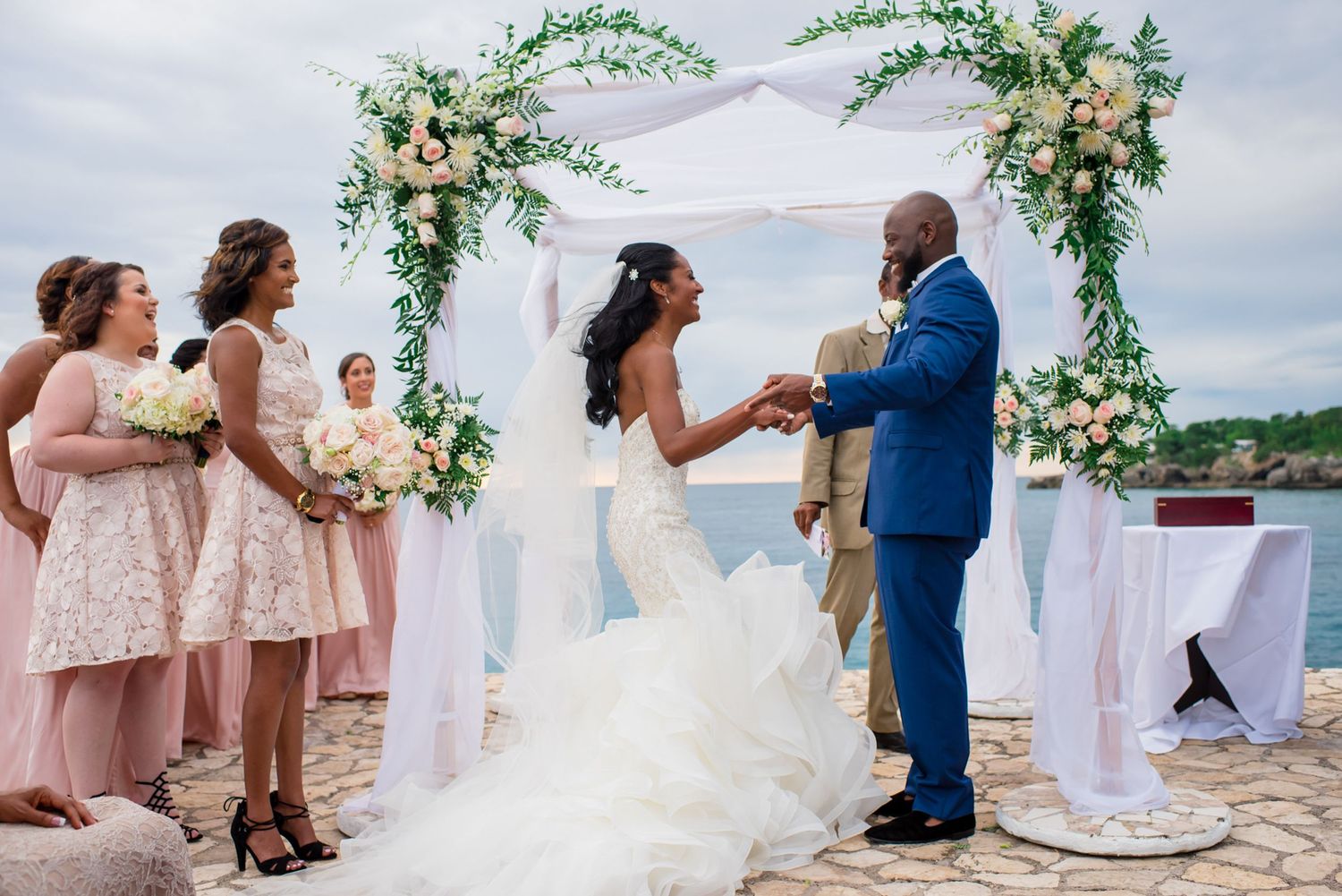 Wedding ceremony on a seaside terrace with bridesmaids in pink dresses and floral arch decorations.