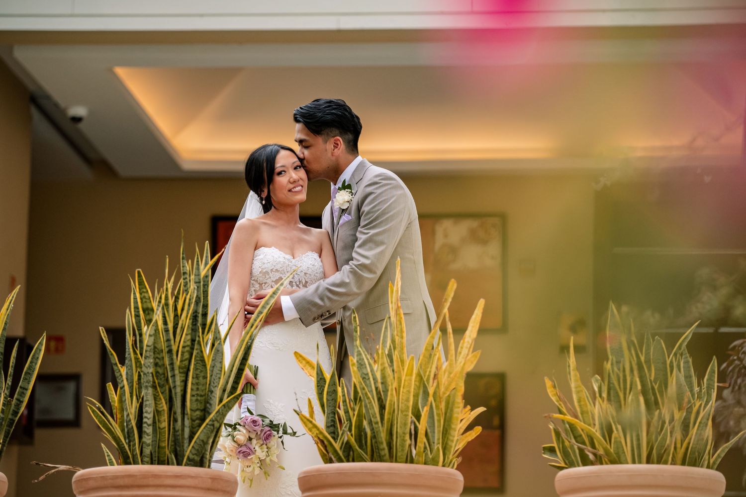 Romantic wedding portraits captured in an indoor venue with lush green plants as backdrop.